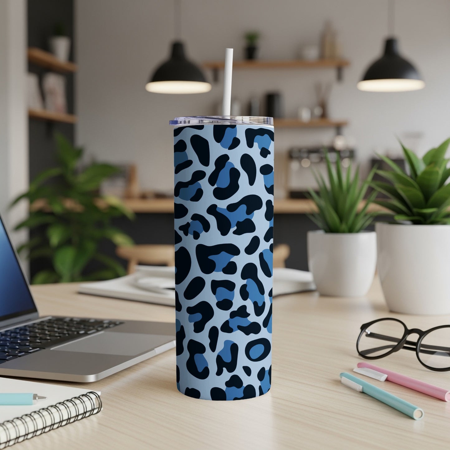 Blue leopard print tumbler with straw on a desk with laptop and plants.