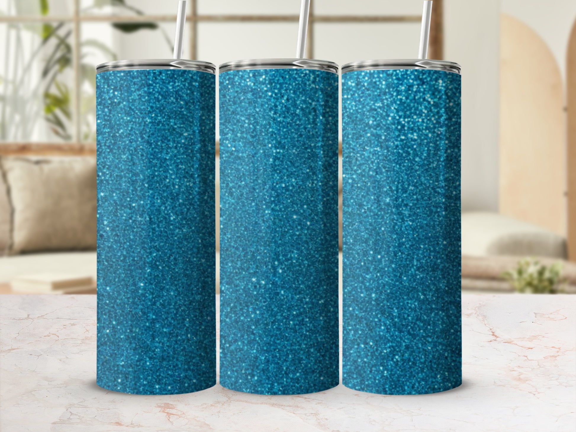 Three glittery blue tumblers with straws on a marble surface.