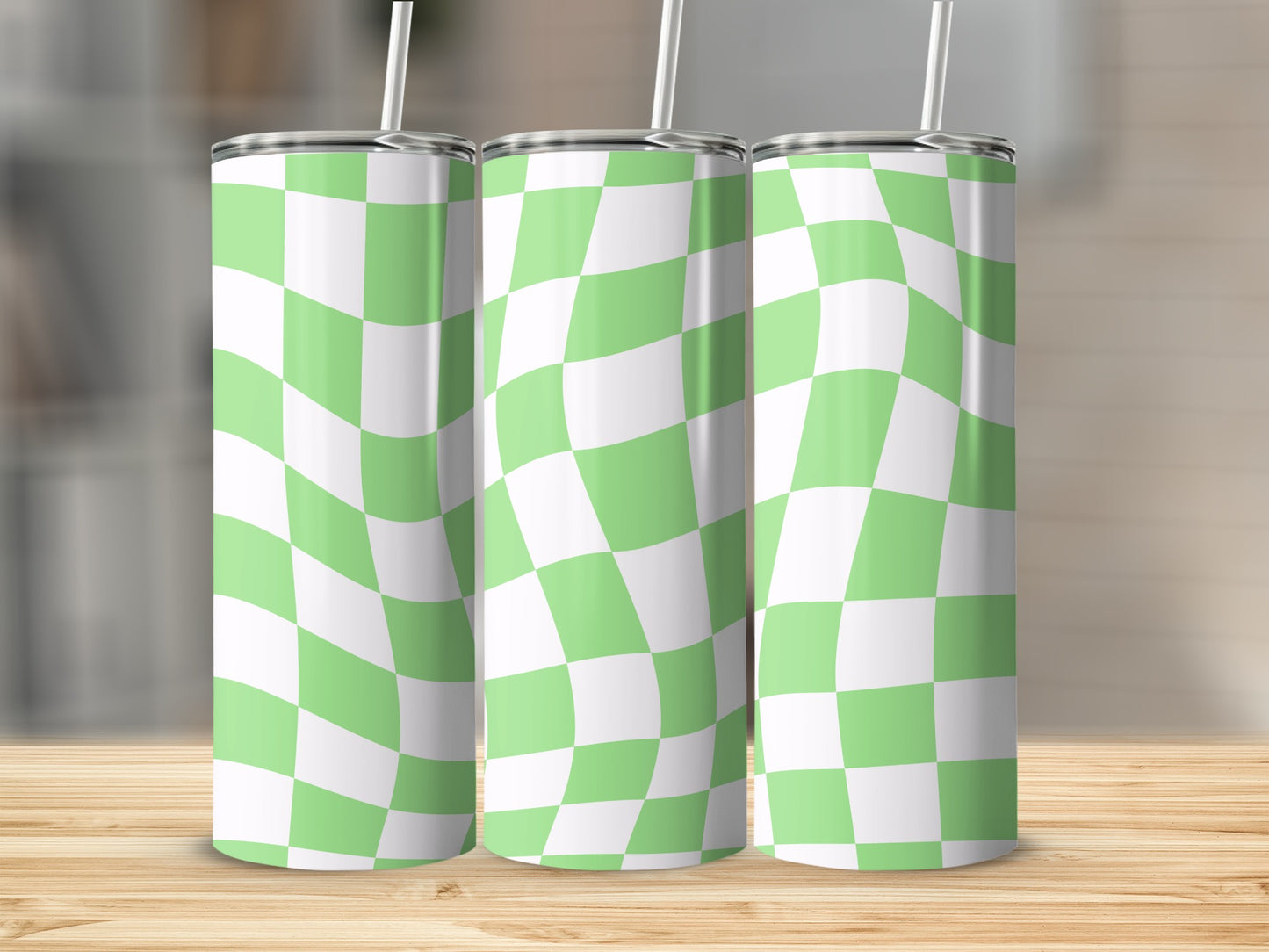 Three green and white checkered tumblers with straws on a wooden surface.