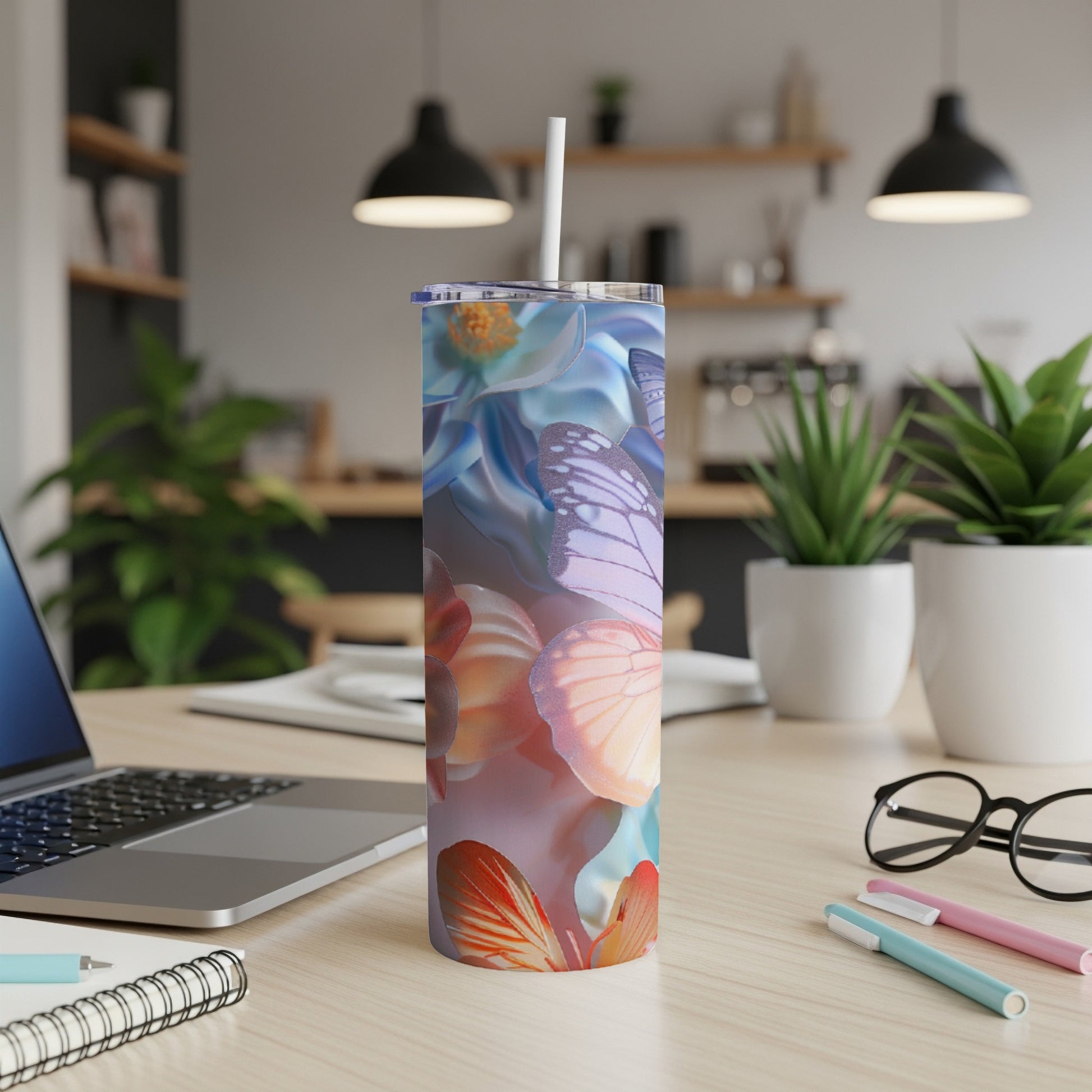 Tumbler with floral and butterfly design on a wooden desk with laptop and pens.