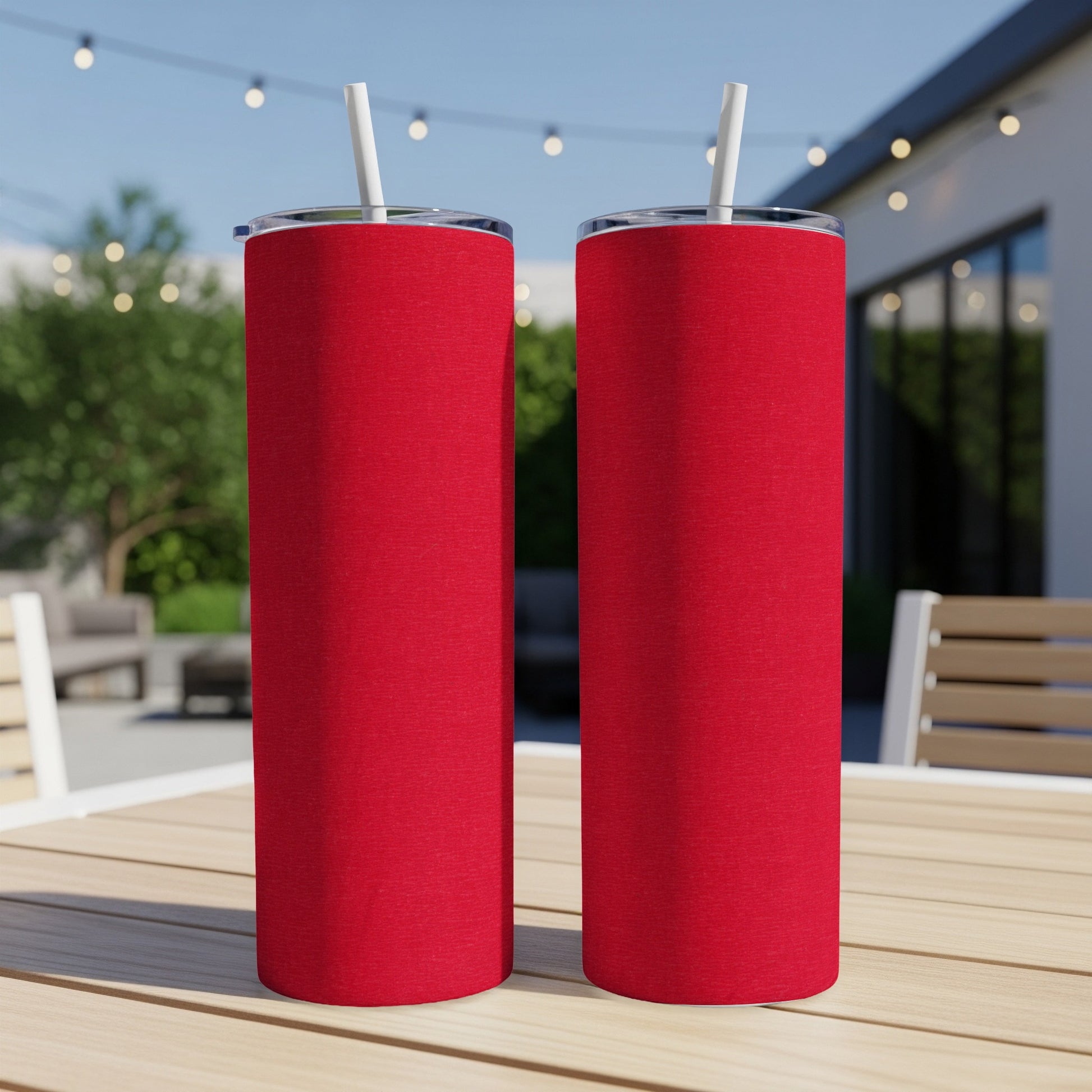 Two red tumblers with straws on a wooden table outdoors.