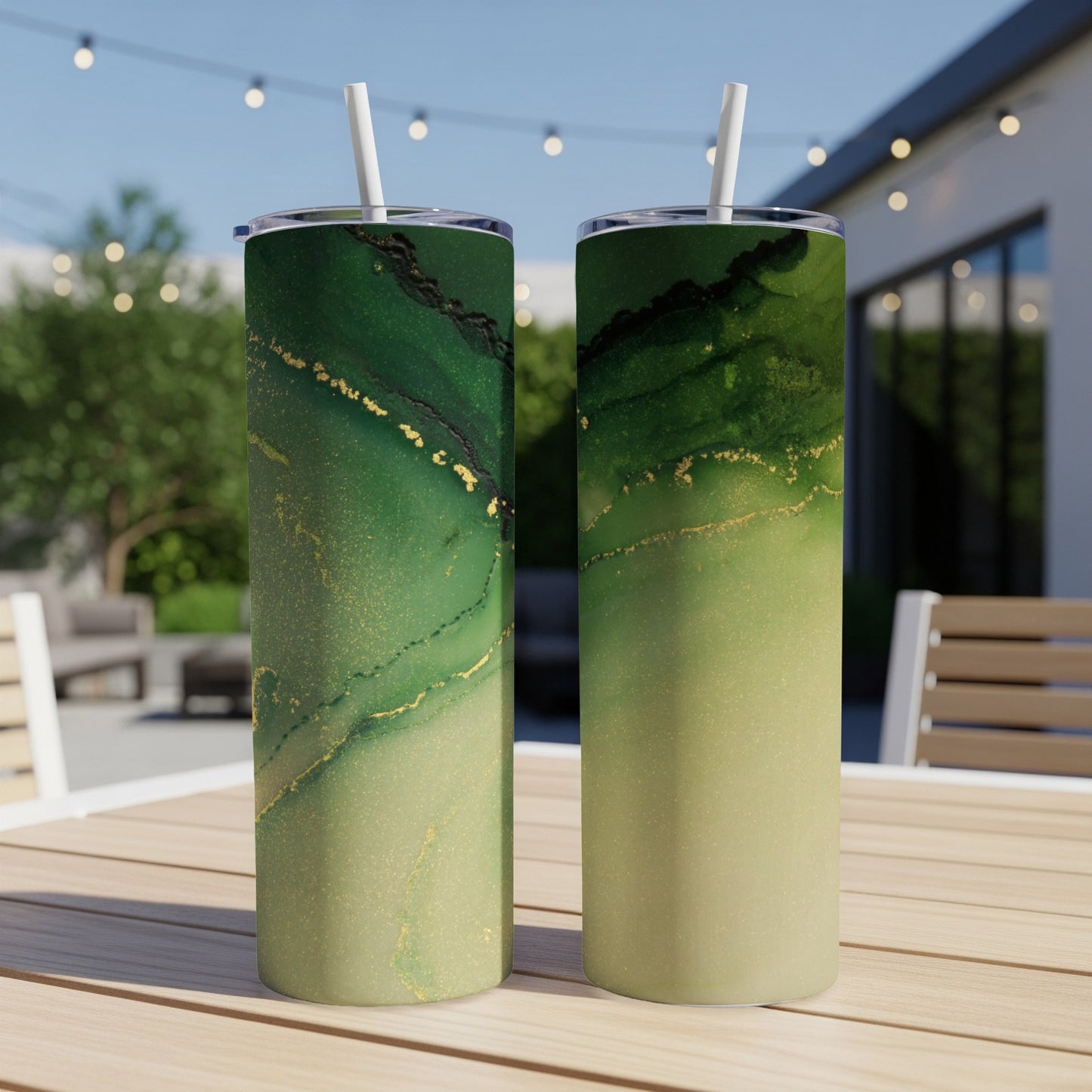 Two green and gold marble-patterned tumblers with straws on a wooden table outdoors.