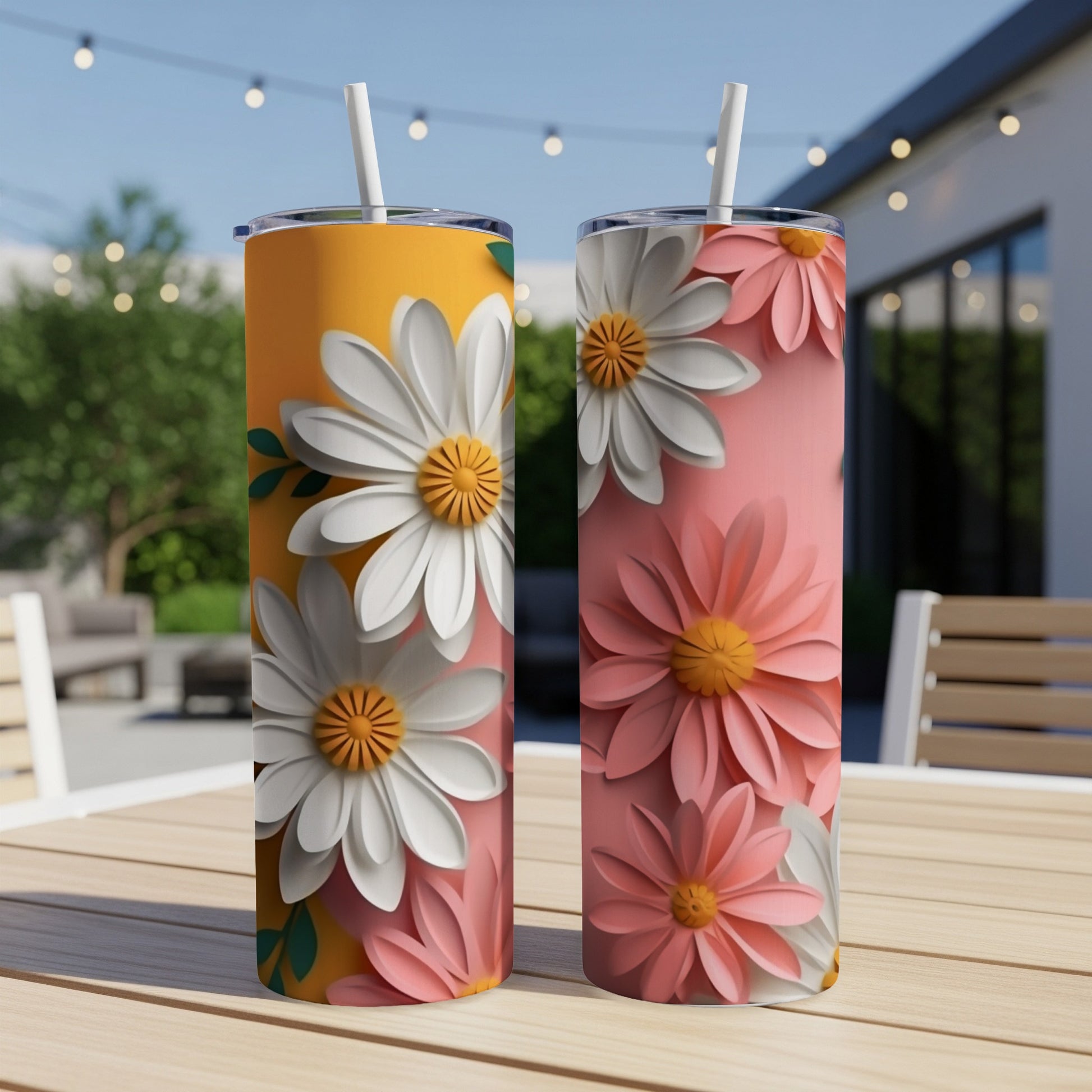 Two tumblers with white and pink daisy designs on an outdoor table.