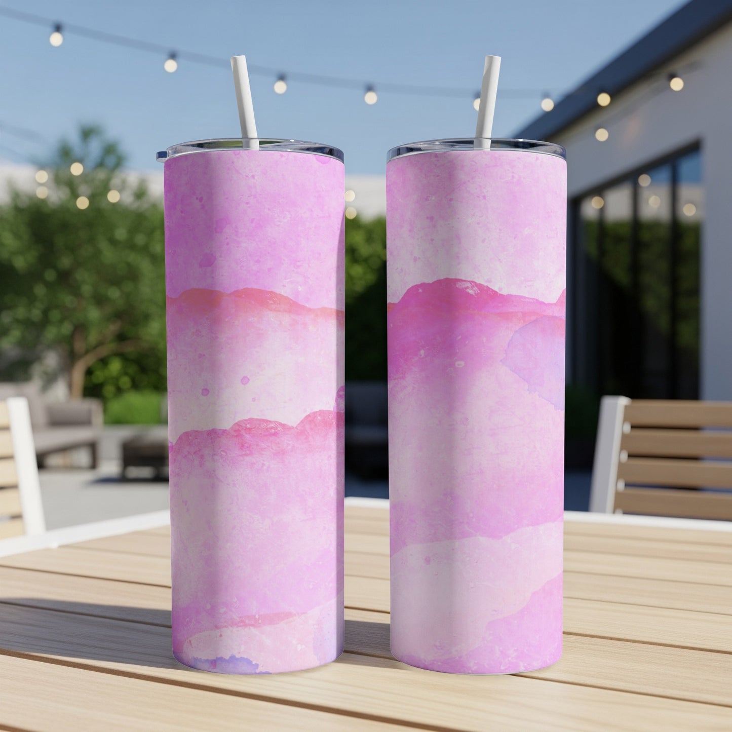 Two pink watercolor tumblers with straws on a wooden table outdoors.