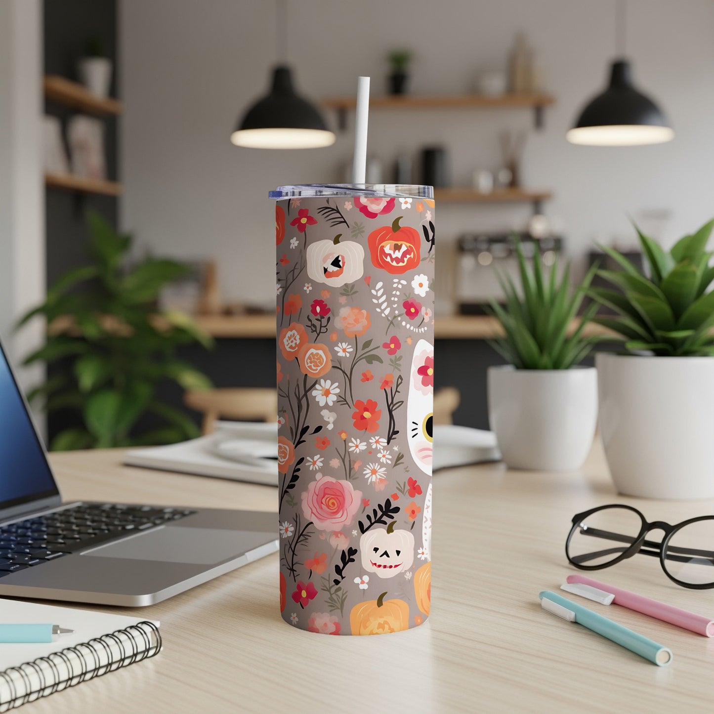 Floral pattern tumbler with pumpkins and a cat face on a desk.