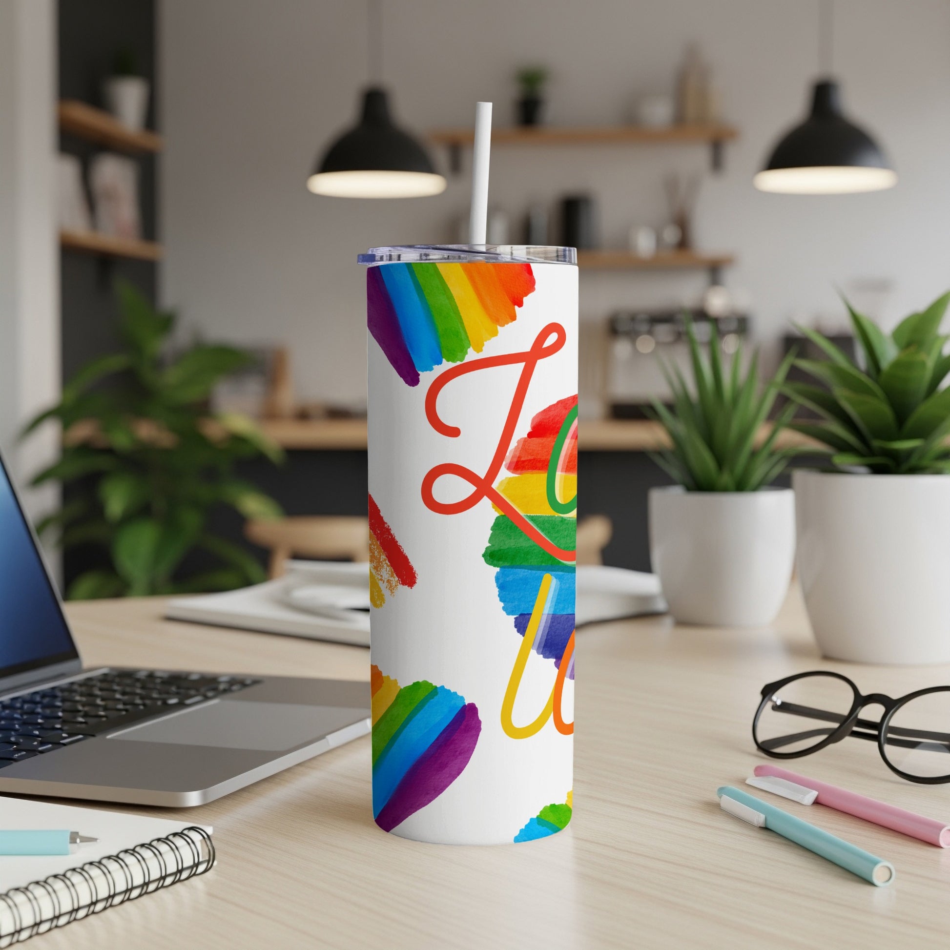 Rainbow "Love" text on white tumbler with straw, desk setting.