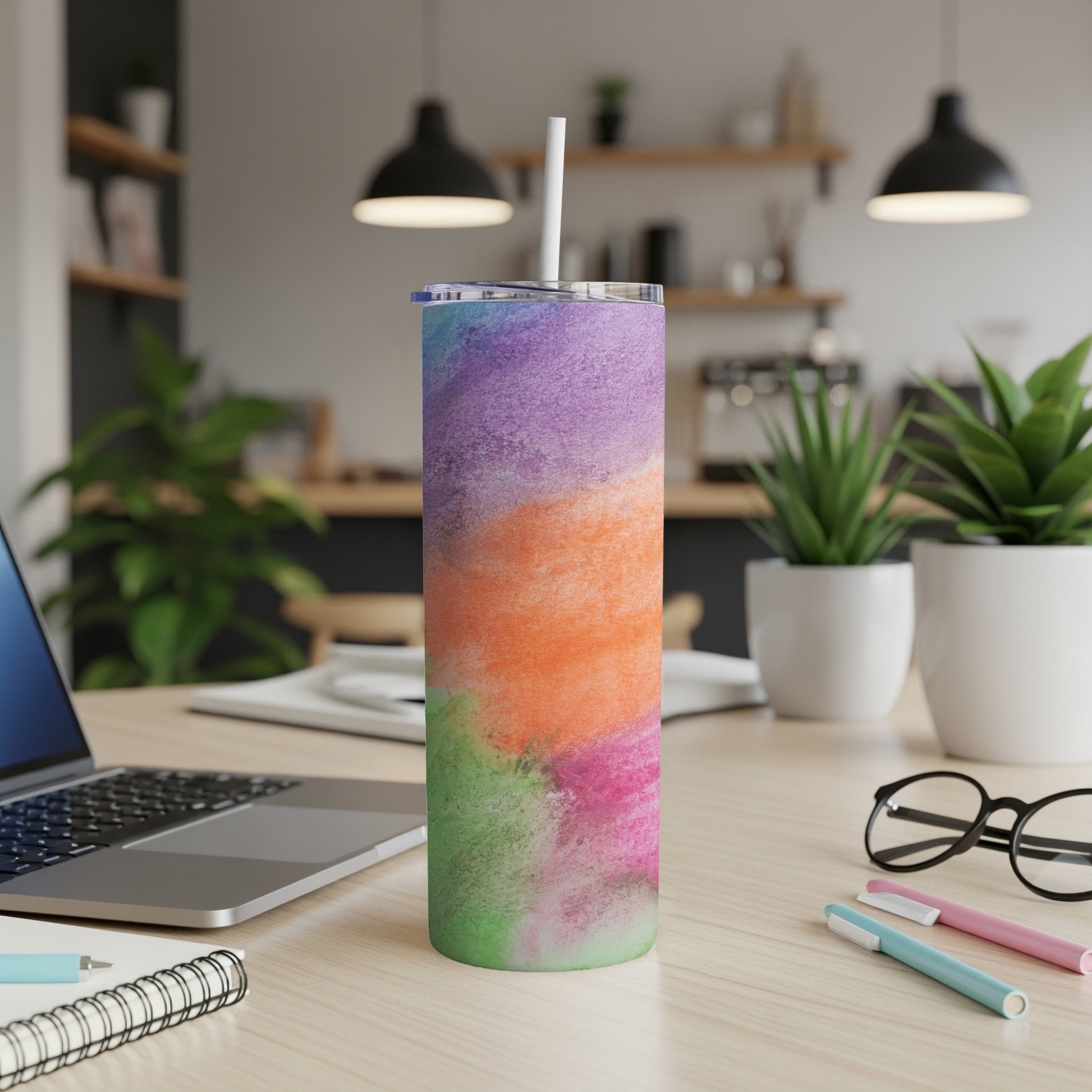Multicolor abstract watercolor tumbler with straw on desk.