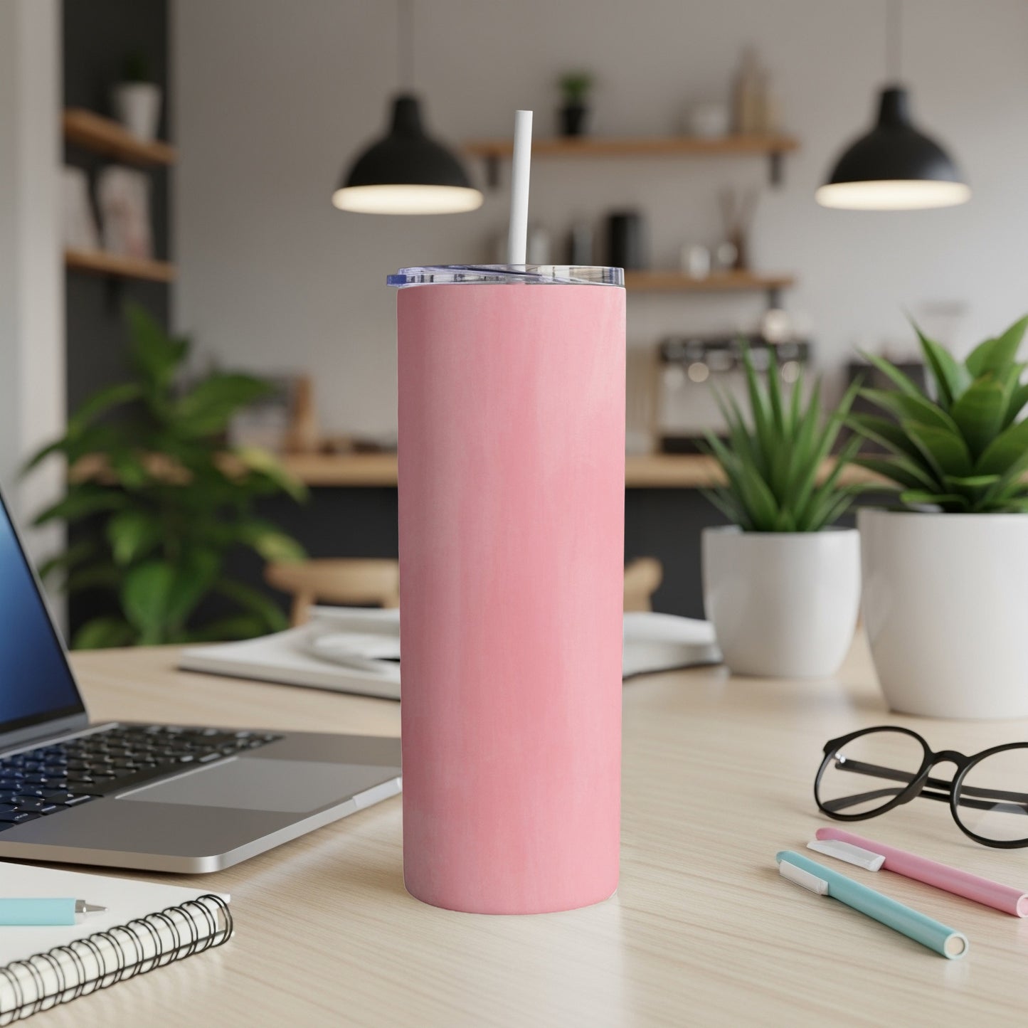 Pink skinny tumbler with white straw on desk with laptop and plants.