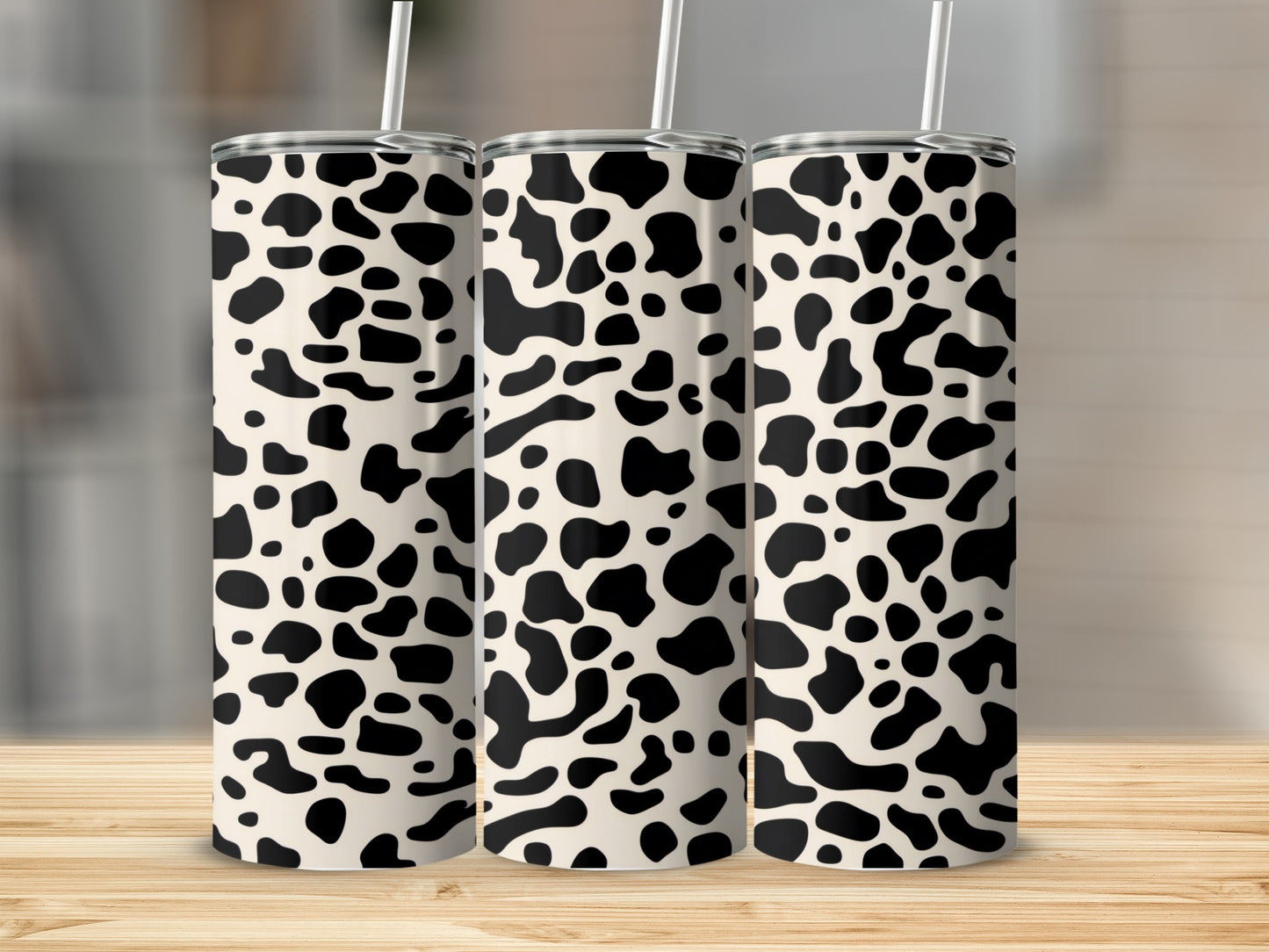 Three cow print tumblers with straws on a wooden surface.