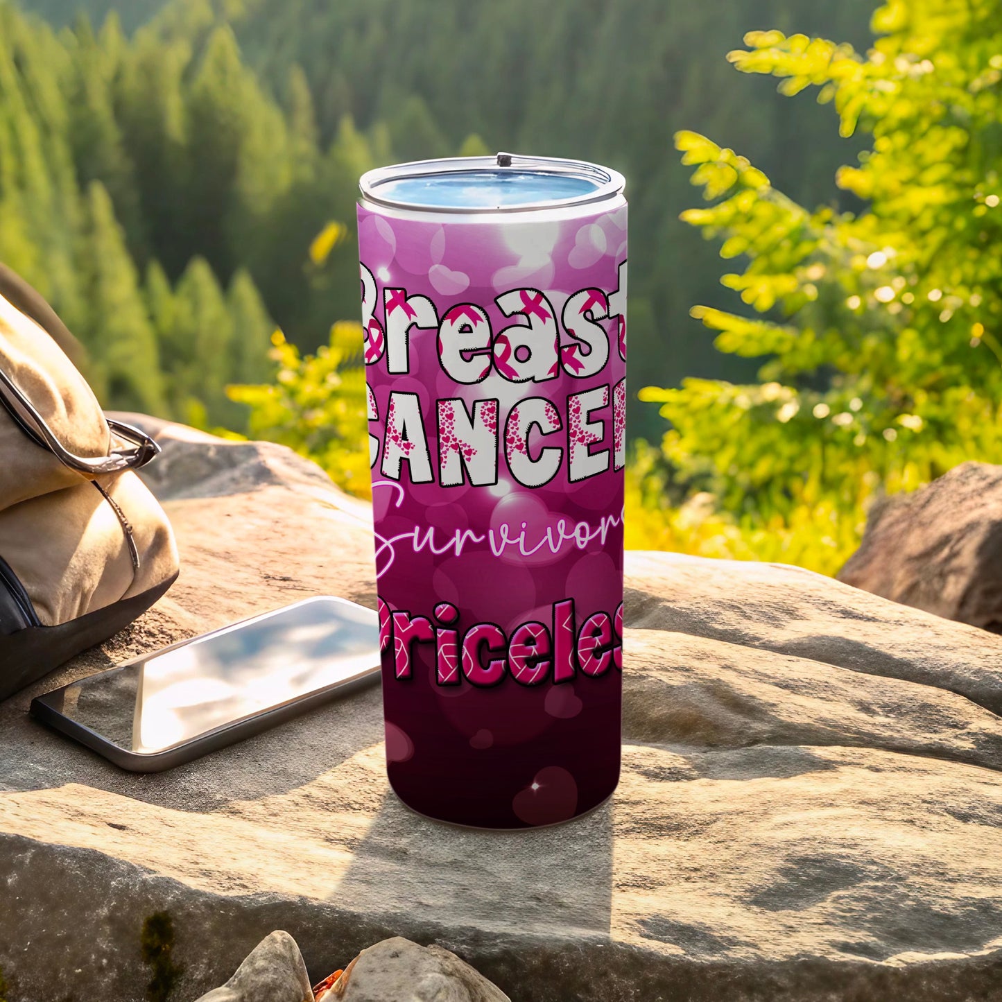Pink tumbler with "Breast Cancer Survivor Priceless" text, resting on rocks outdoors.