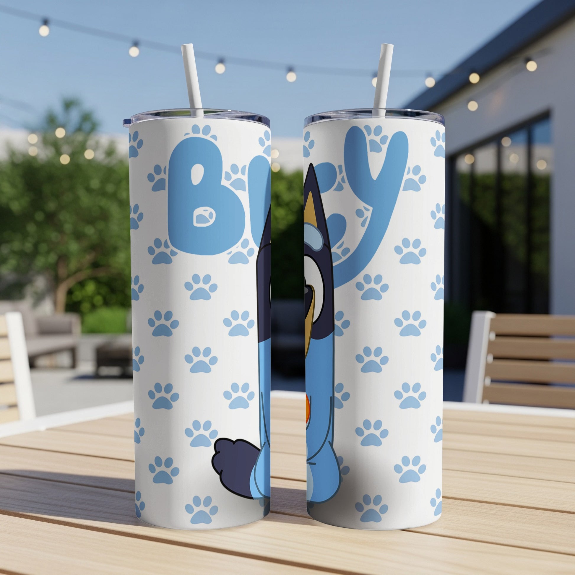 Two Bluey character tumblers with paw print pattern on outdoor table.