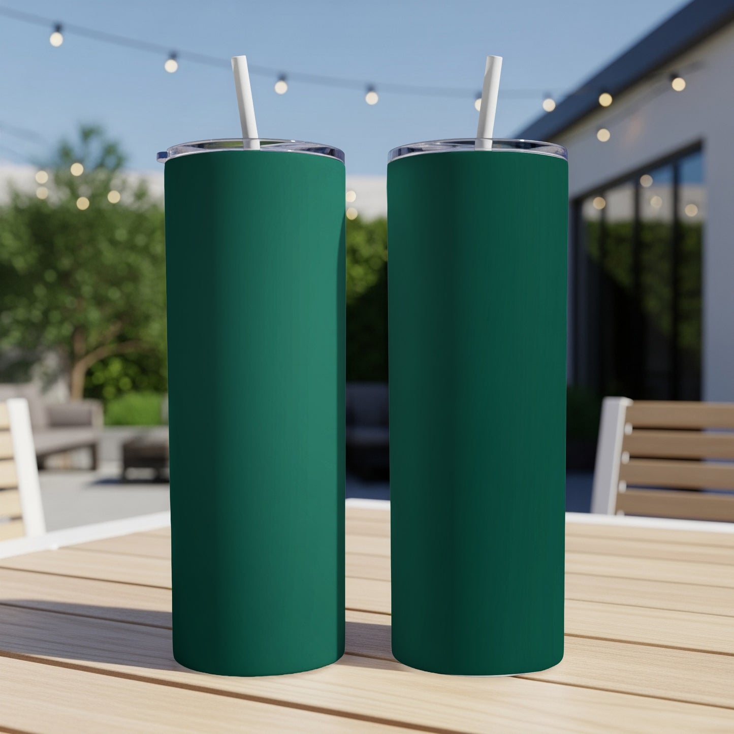 Two green tumblers with white straws sit on a wooden table outdoors.