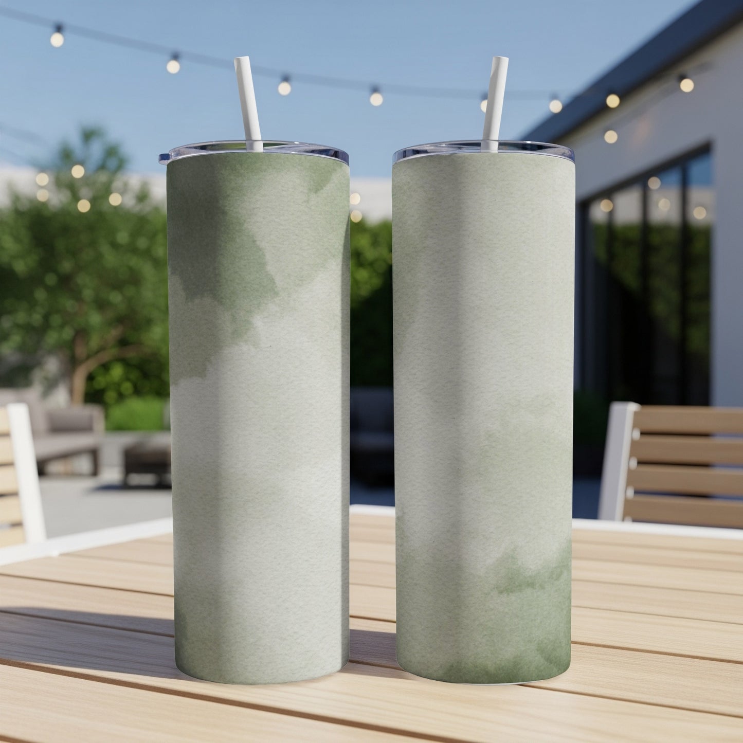 Two tall tumblers with a watercolor pattern sit on a wooden table outdoors.