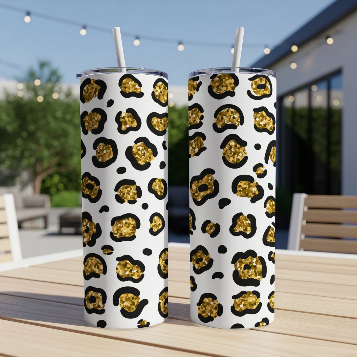 Two white tumblers with a gold leopard print pattern and straws on a table.