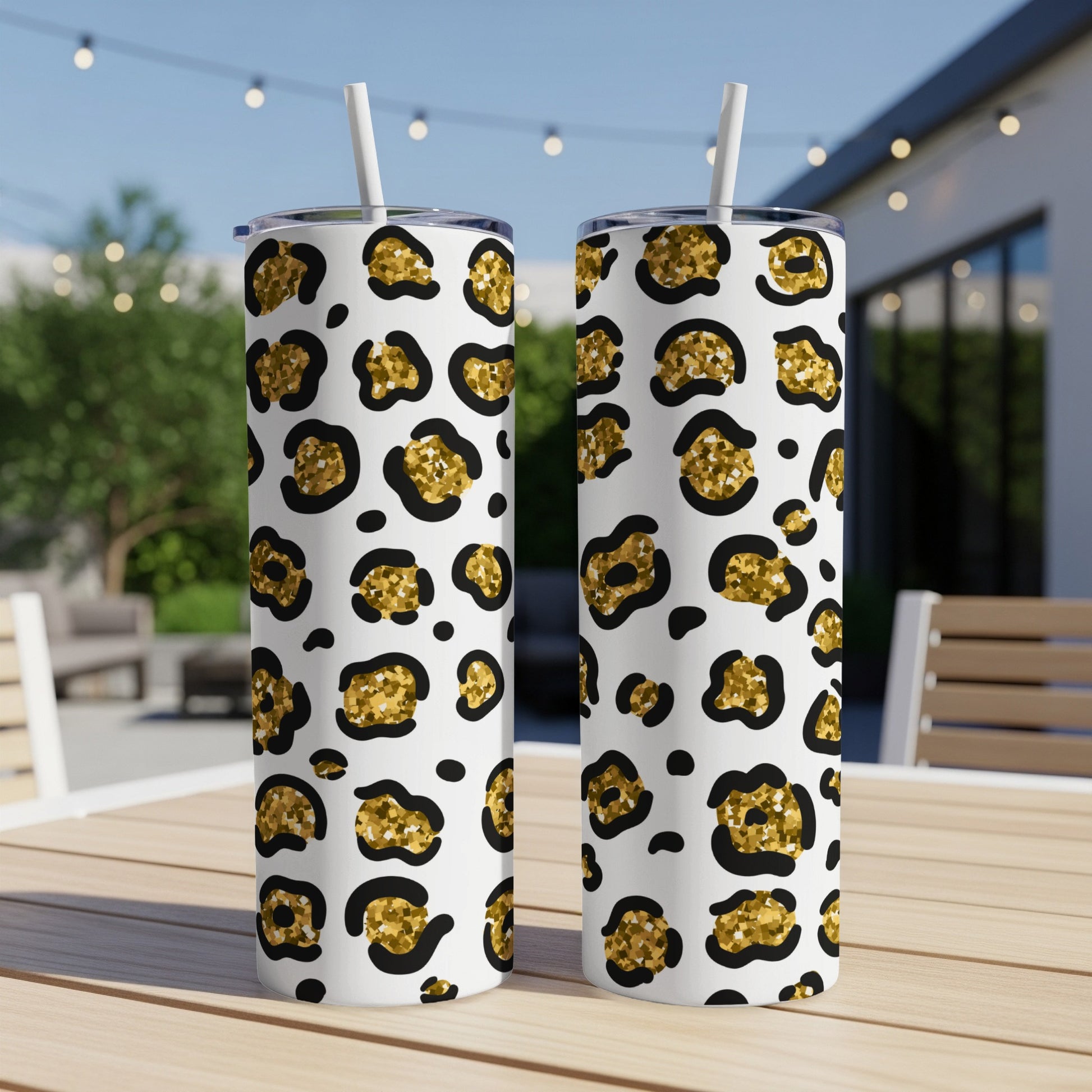 Two white tumblers with a gold leopard print pattern and straws on a table.