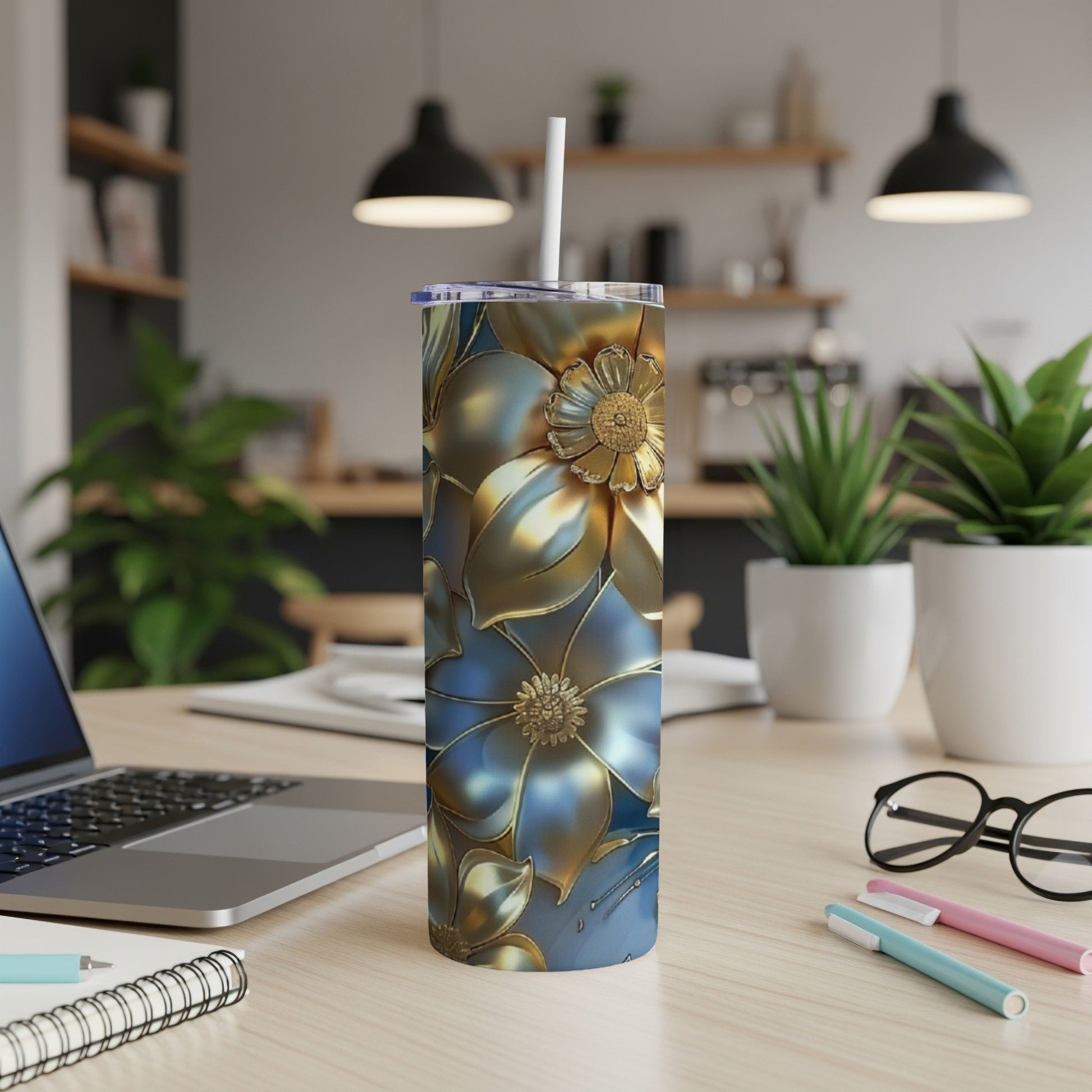Gold and blue floral tumbler with straw on a desk.