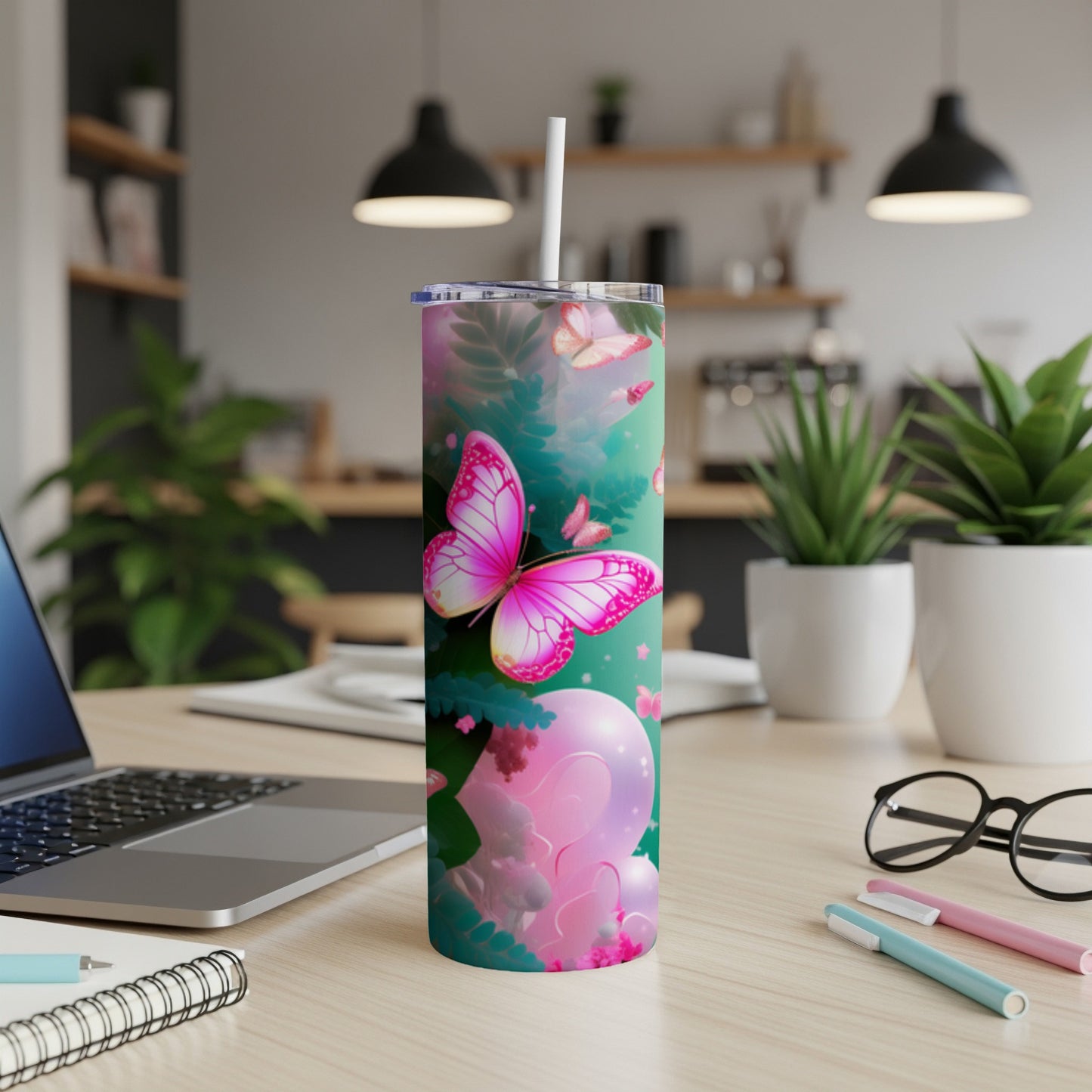 Pink butterfly tumbler with straw on desk near laptop and pens.
