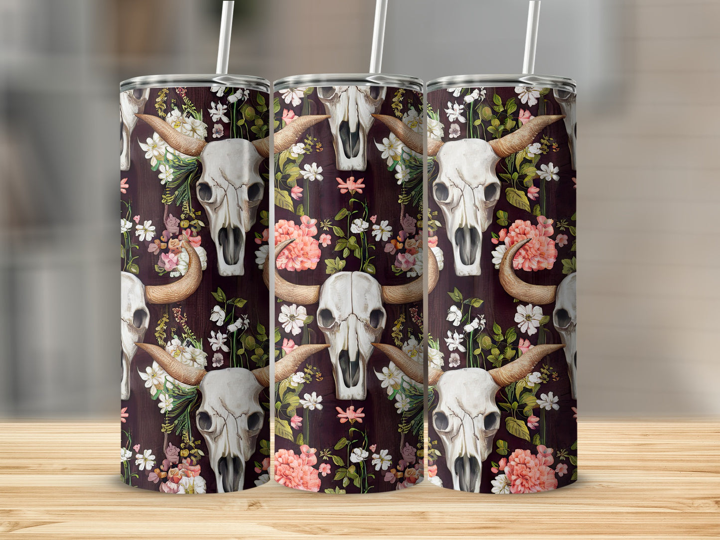 Skull and floral pattern on three tumblers with straws on a wooden surface.