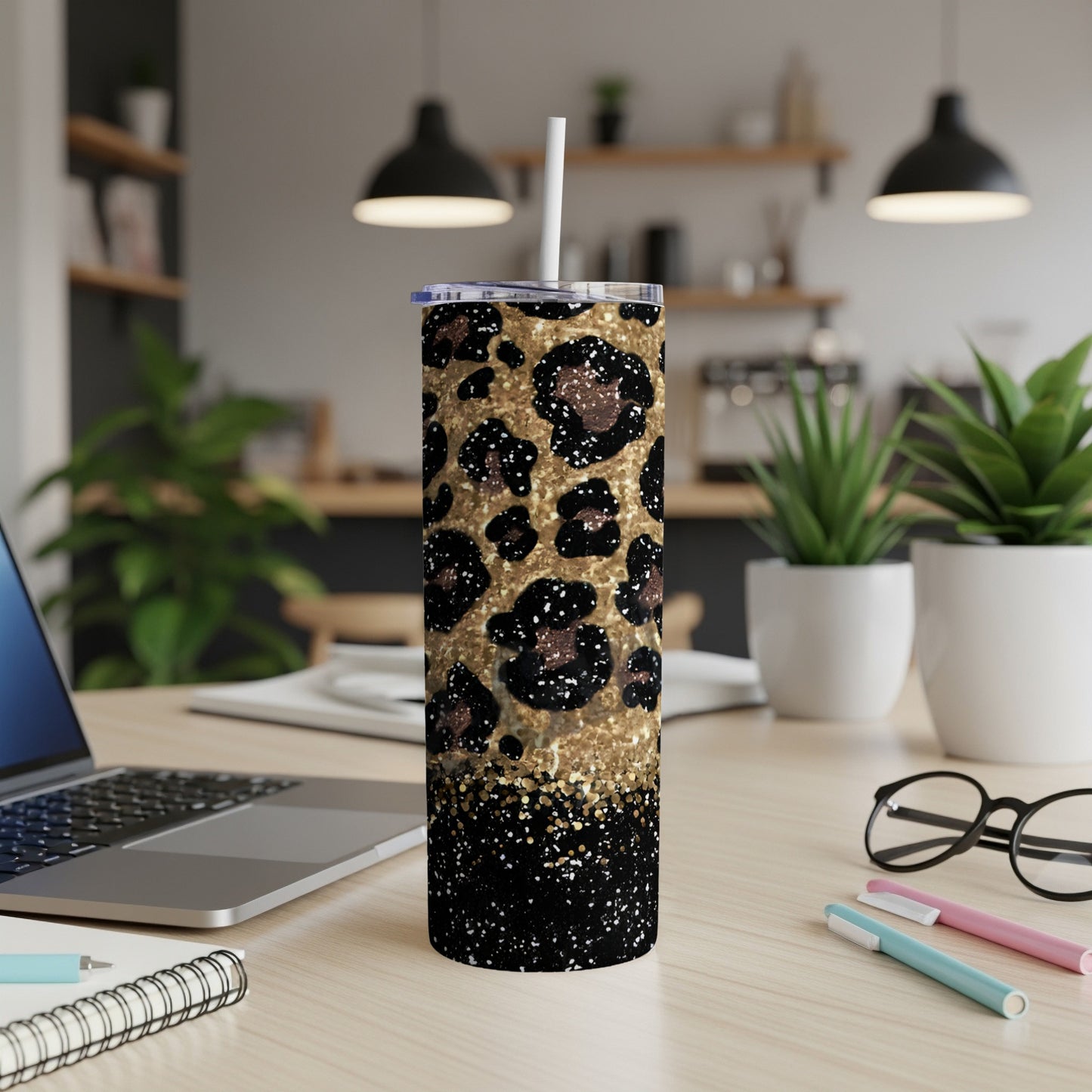 Glittering leopard print tumbler with straw on a desk with laptop and pens.