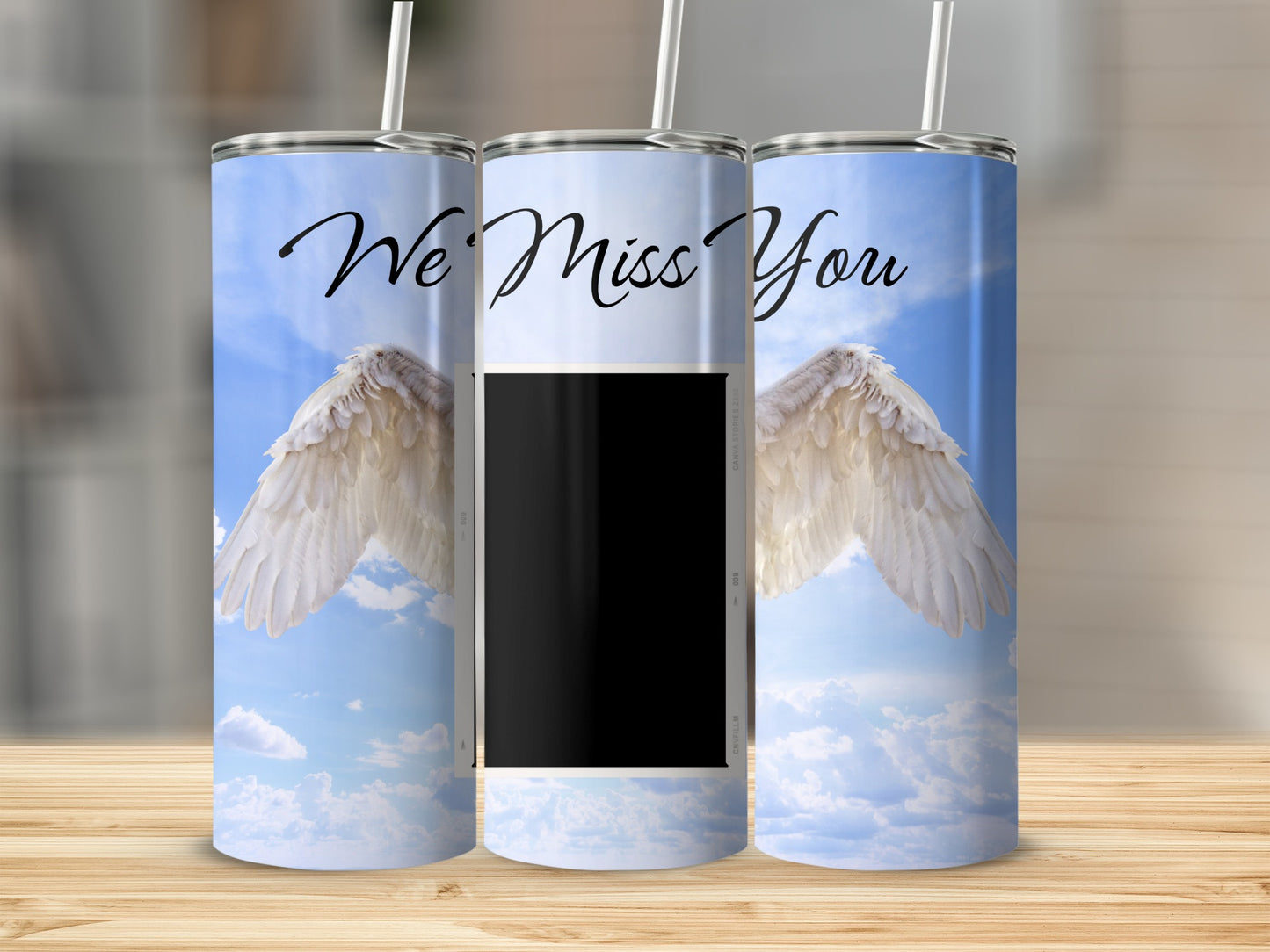 "We Miss You" text with angel wings and a photo frame on a sky background.