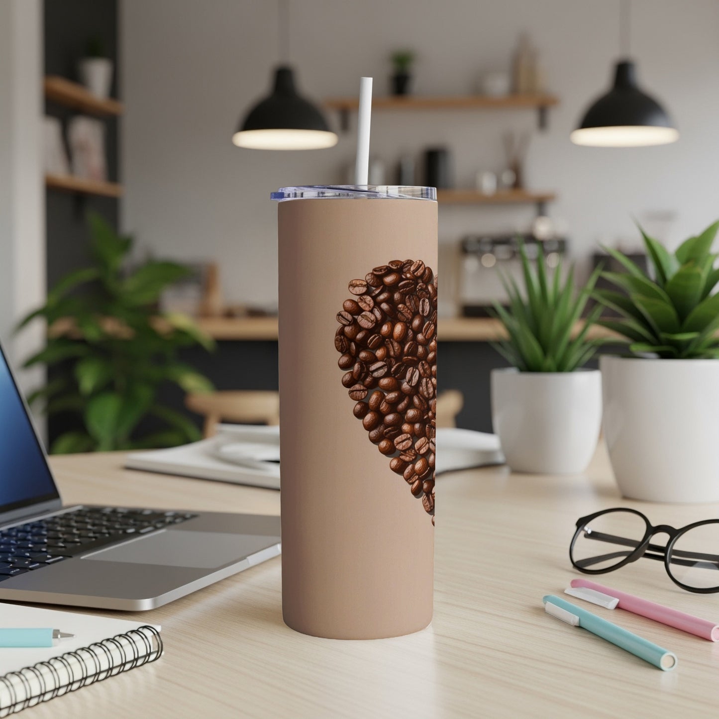 Brown tumbler with heart shape of coffee beans, laptop, and pens.