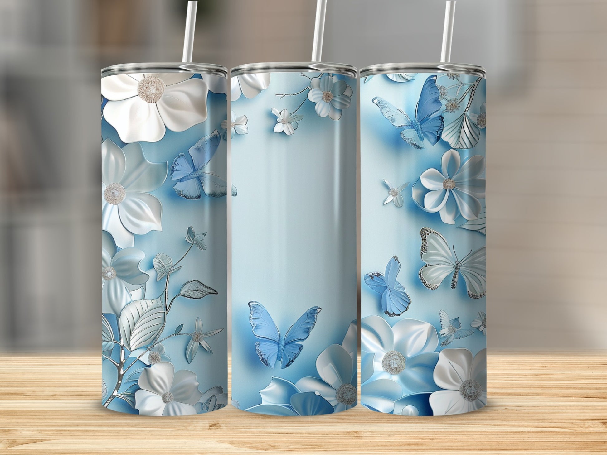 Three blue tumblers with white floral and butterfly designs on a wooden surface.