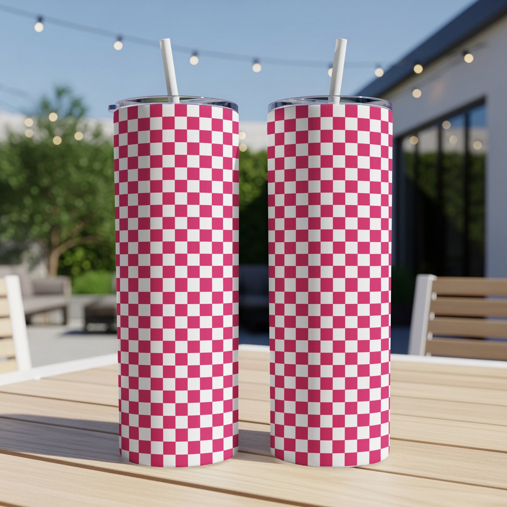Two pink and white checkered tumblers with straws on a wooden table.