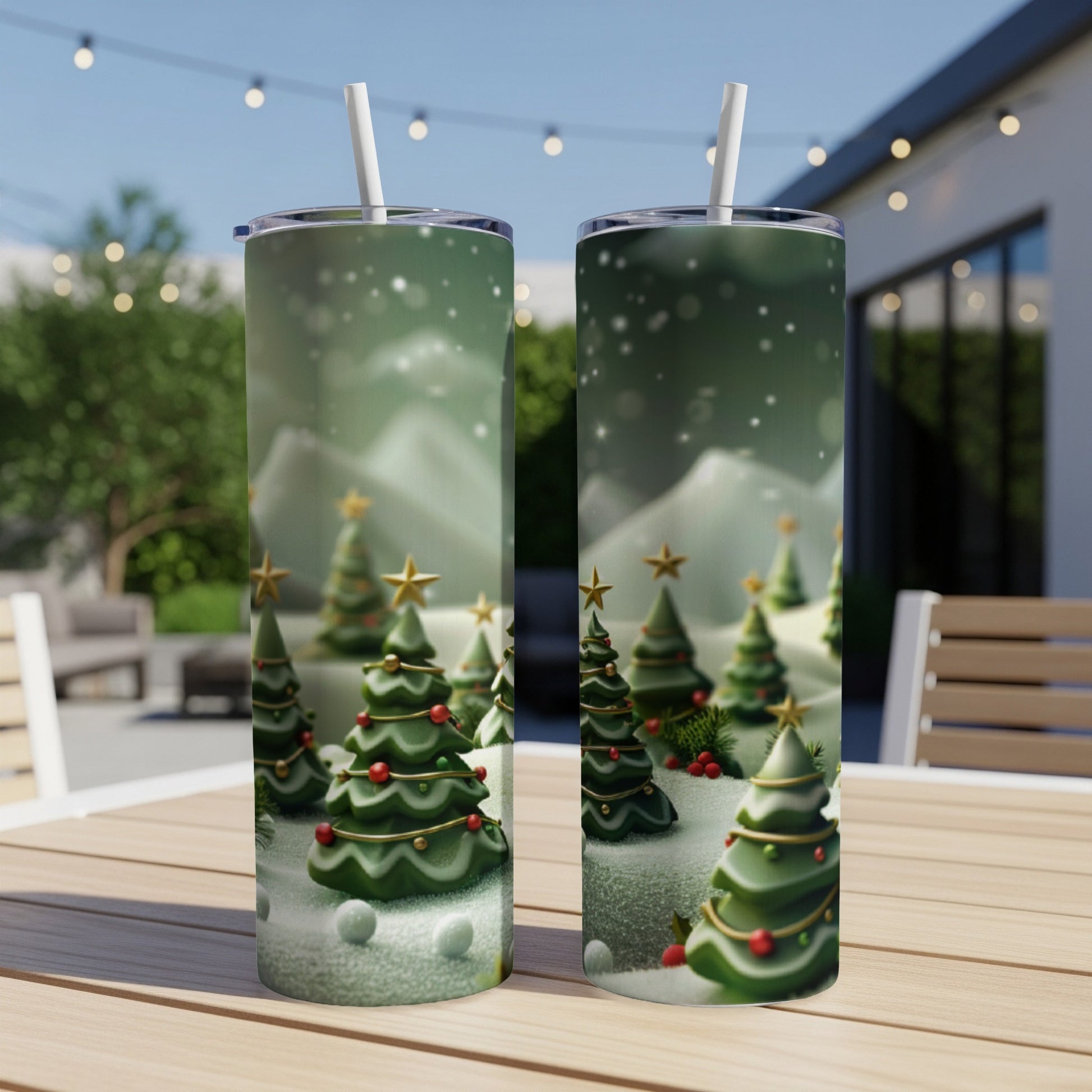 Two tumblers with a Christmas tree forest design, white straws, on a wooden table outdoors.