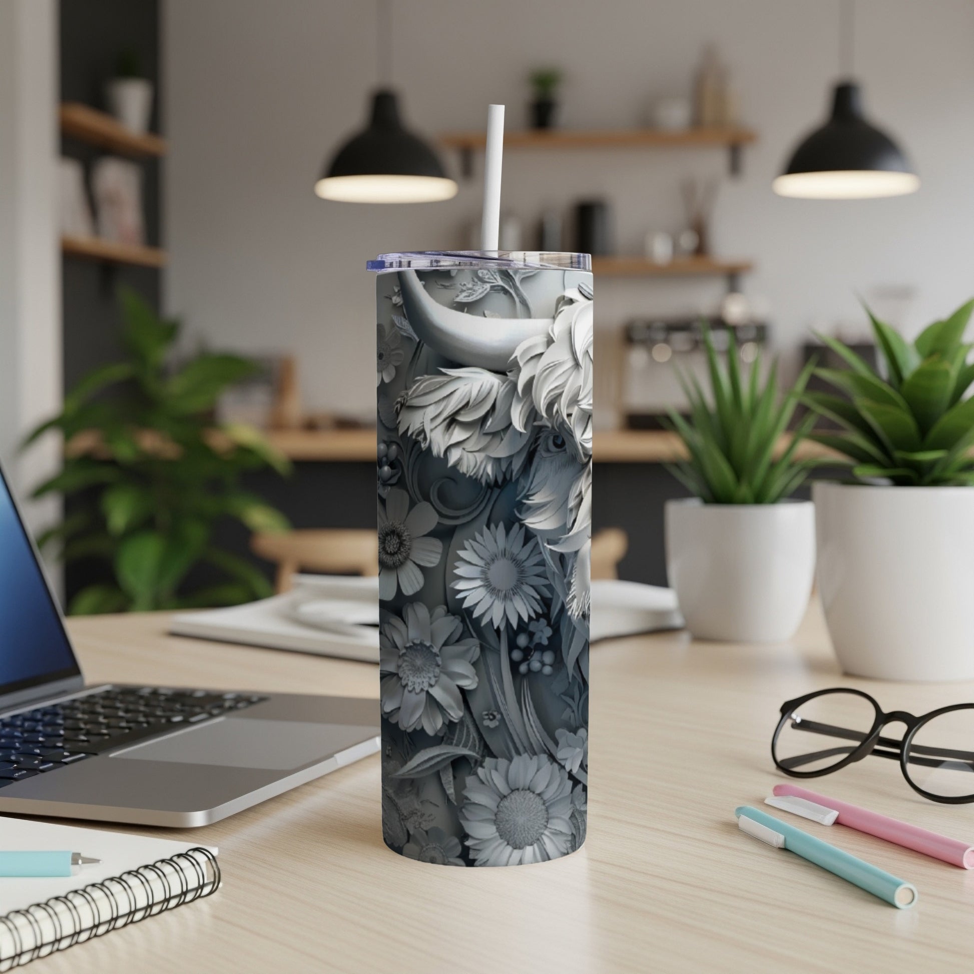 Gray sculpted tumbler with floral and animal designs on a desk.
