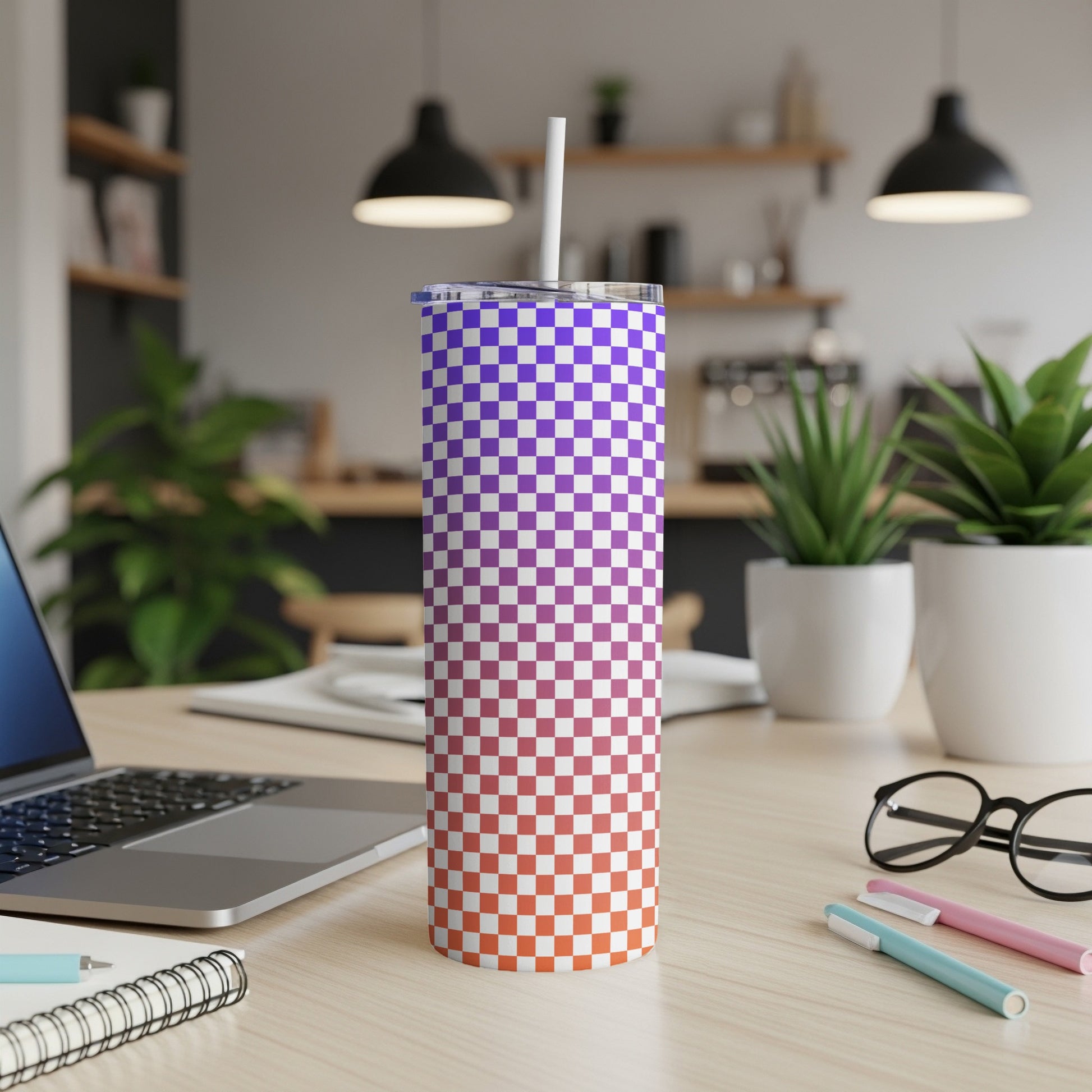 Checkerboard tumbler with purple and orange gradient on desk with laptop and pens.