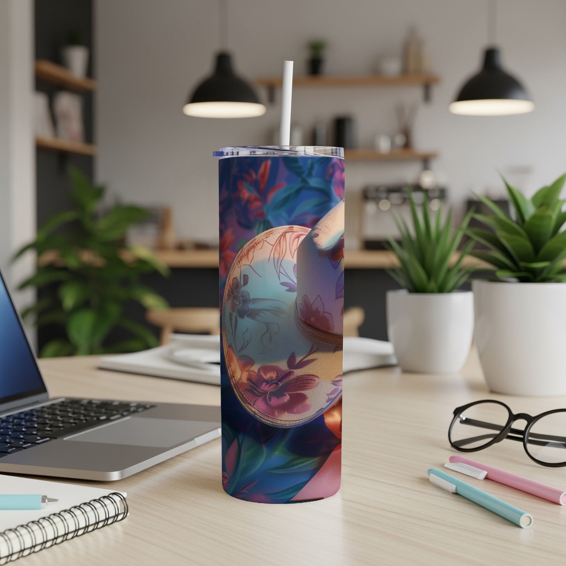 Floral tumbler with straw on desk next to laptop and supplies.