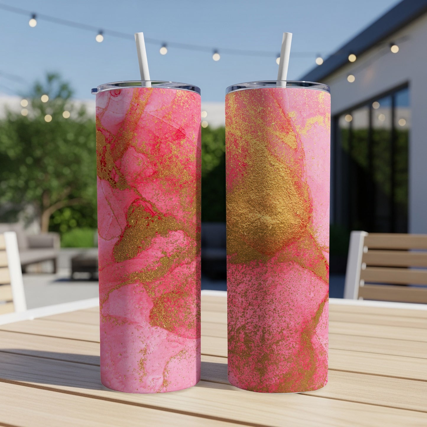 Two pink and gold marbled tumblers with straws on a wooden table.