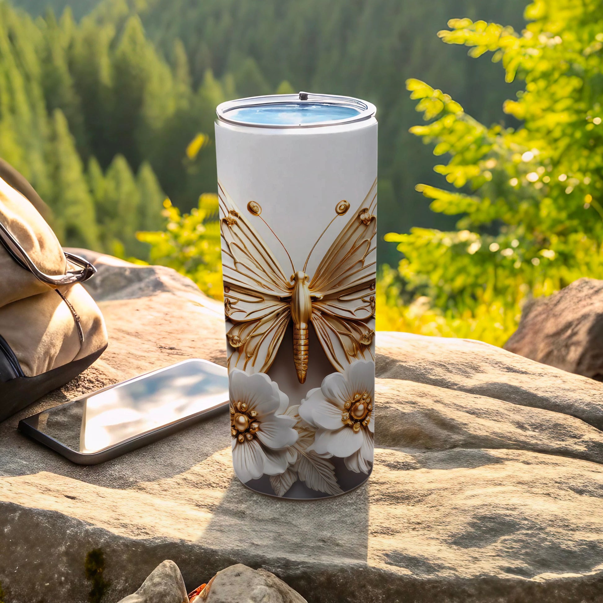 White tumbler with gold butterfly and floral design on rocky surface.
