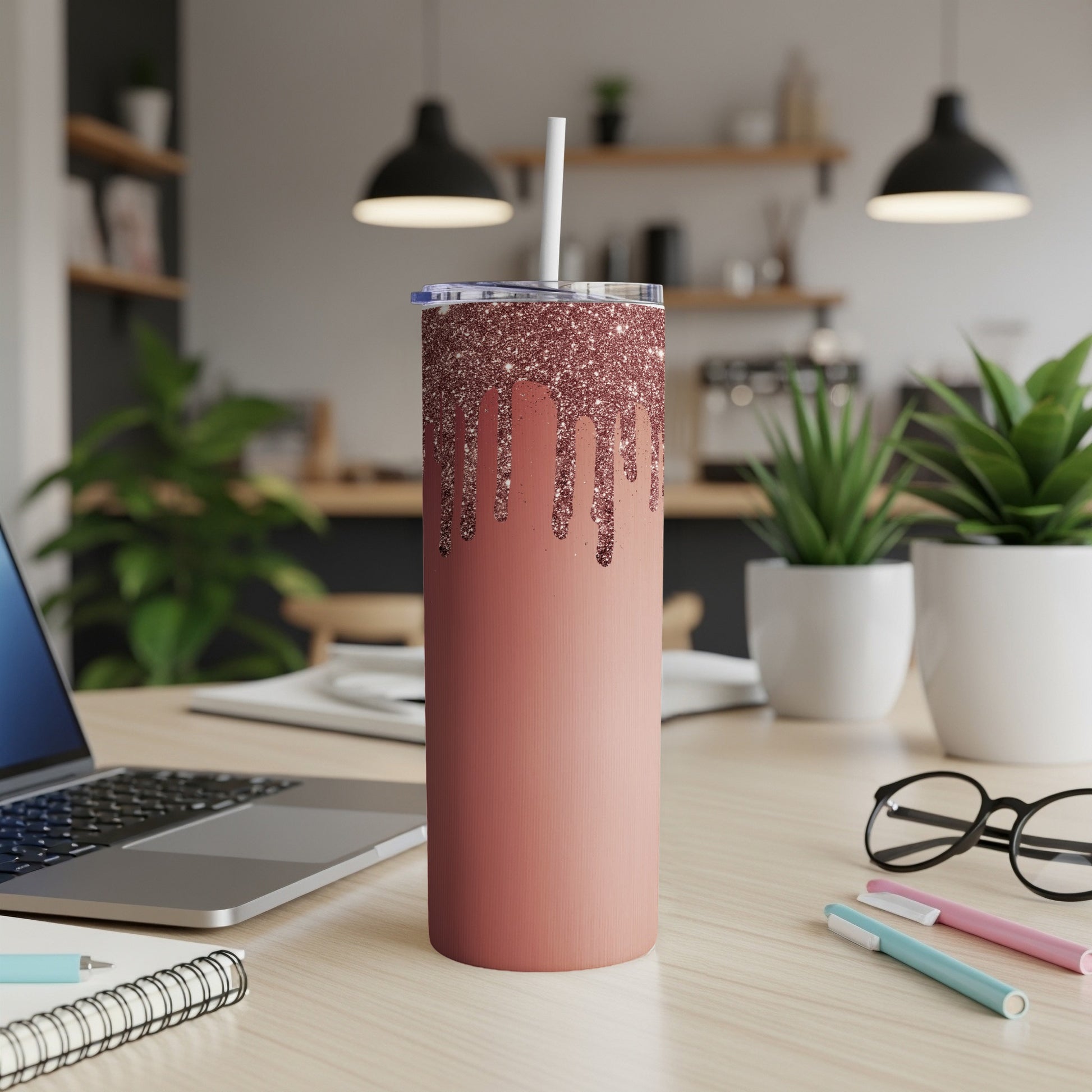 Rose gold glitter drip tumbler with straw on a desk.