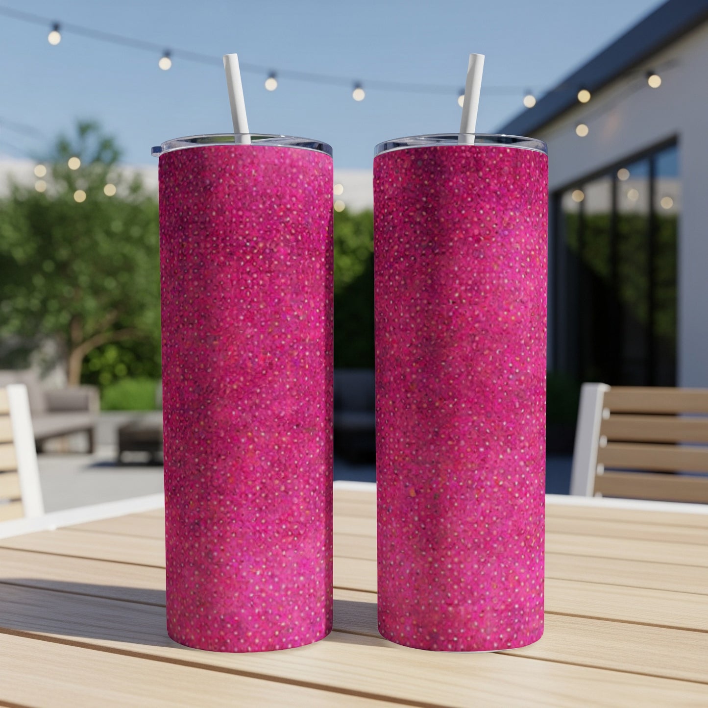 Two pink glitter tumblers with straws on a table outdoors.