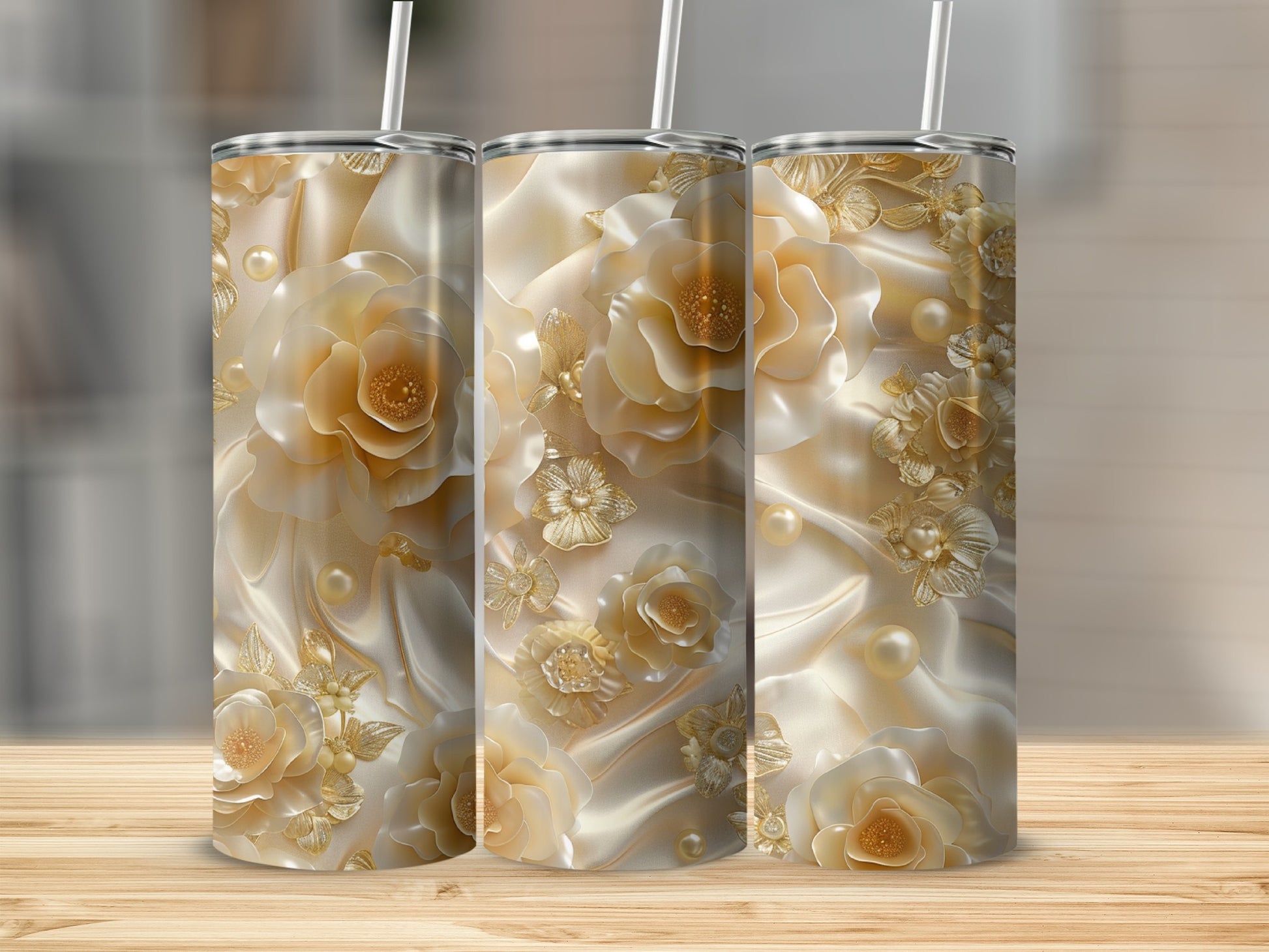 Three gold floral tumblers with pearls and satin fabric on a wooden surface.