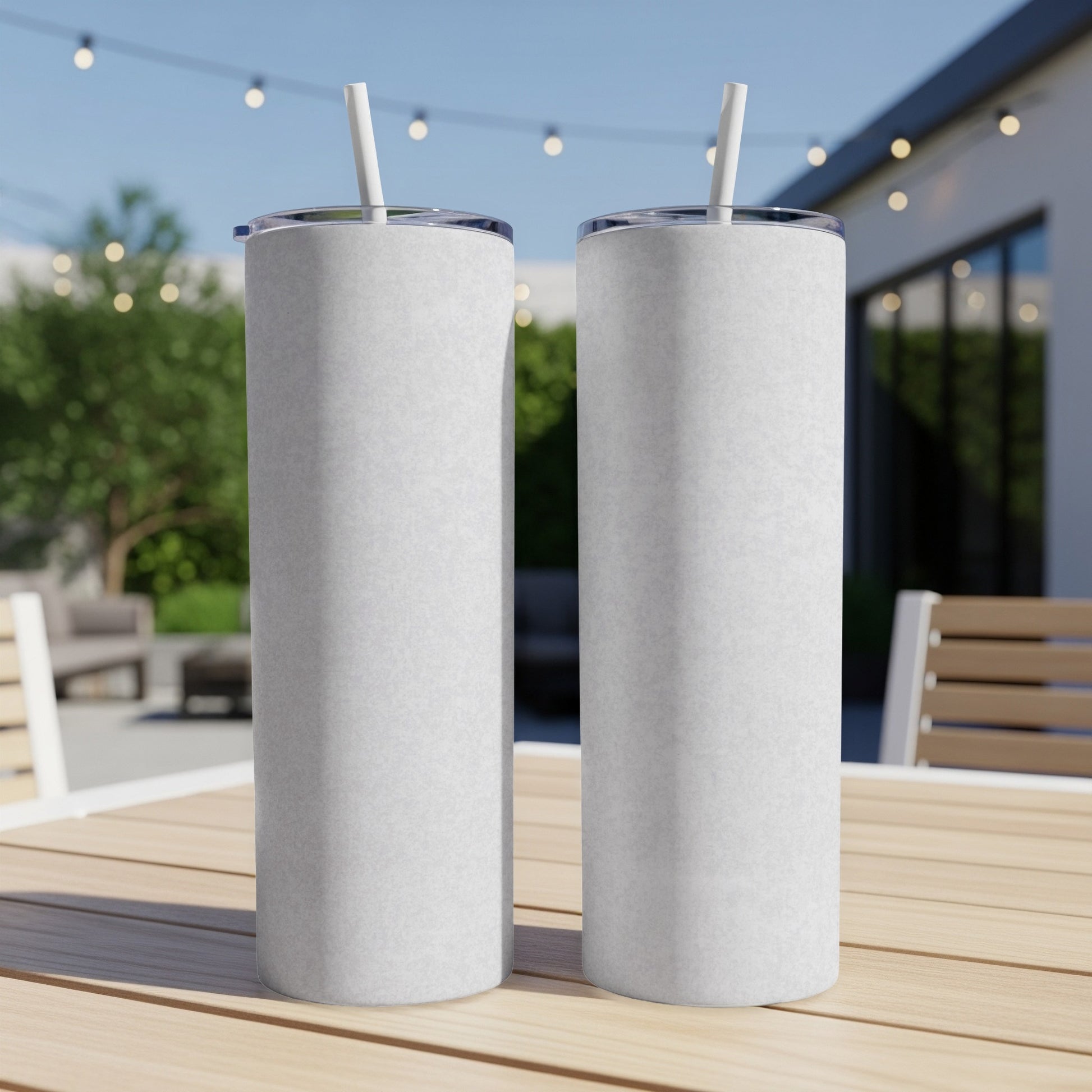 Two blank white tumblers with straws sit on a wooden table outdoors.