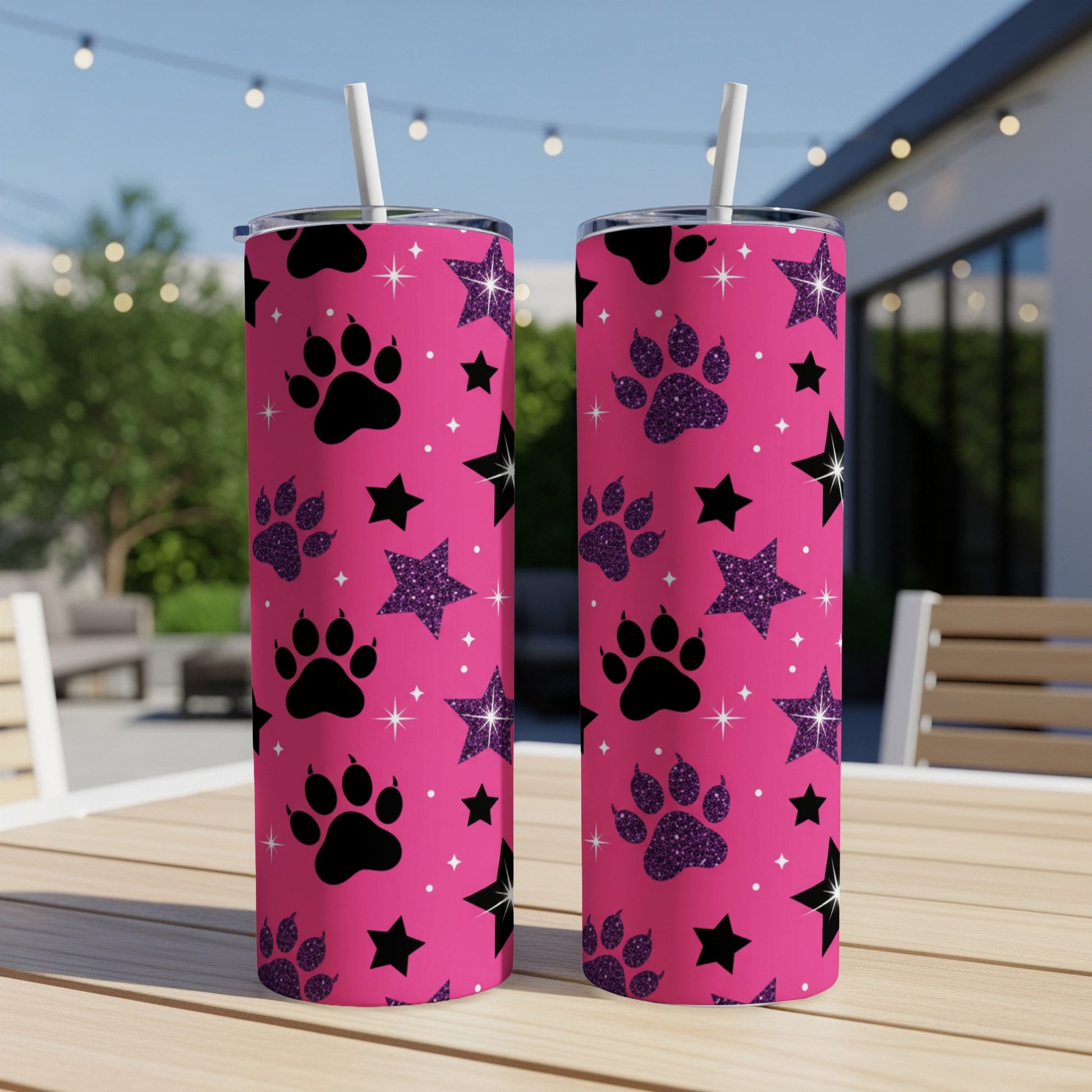 Two pink tumblers with paw prints and glitter stars, on a wooden table.