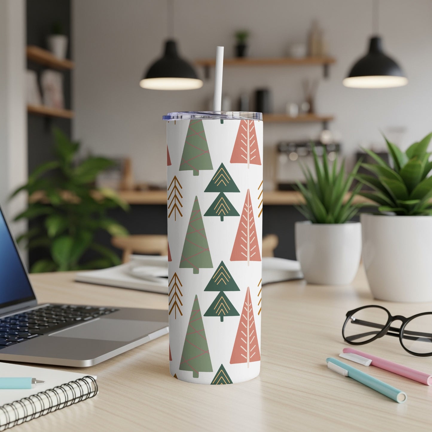 White tumbler with green and pink Christmas tree pattern, on a desk.