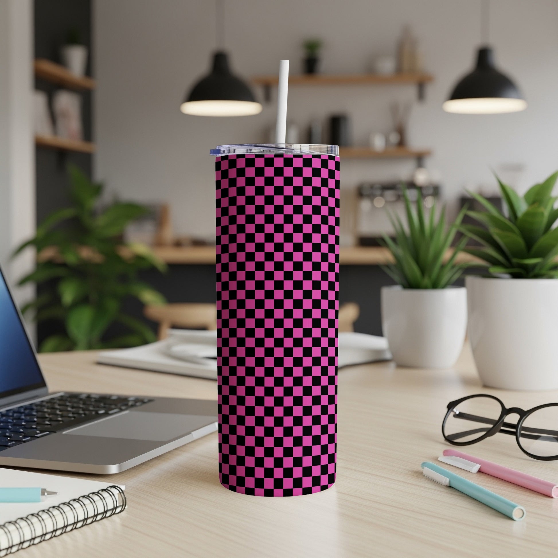Pink and black checkered tumbler with a straw on a desk.