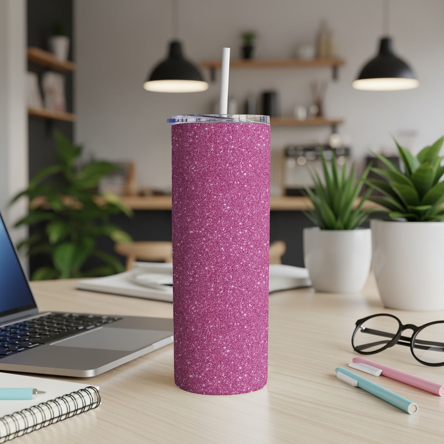 Glittery pink tumbler with straw on a desk next to a laptop.