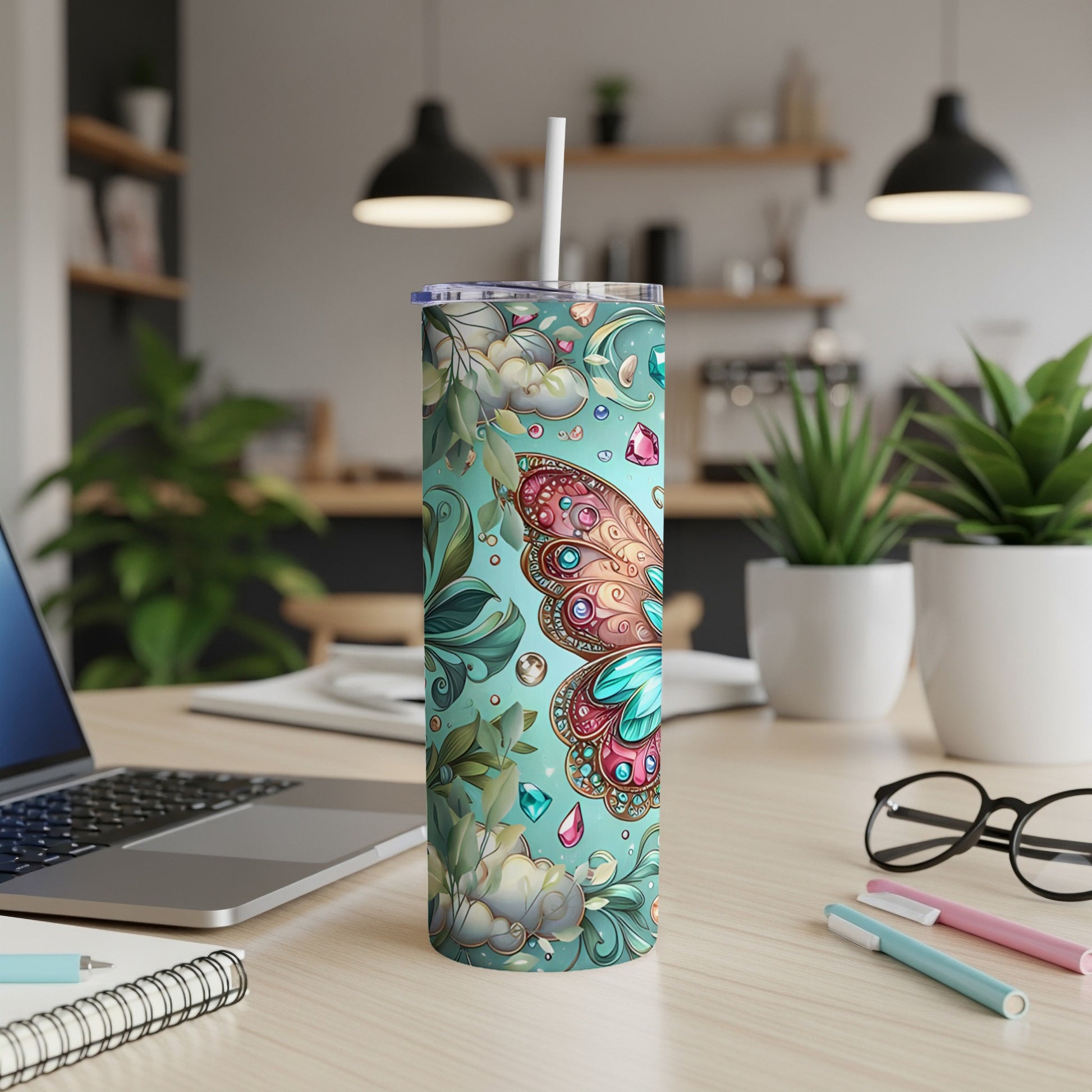 Turquoise tumbler with butterfly and floral design, straw, laptop, and pens.