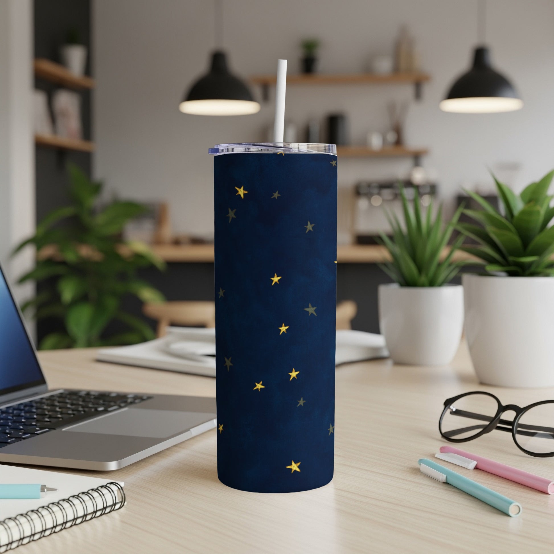 Dark blue tumbler with gold stars and white straw on a desk.