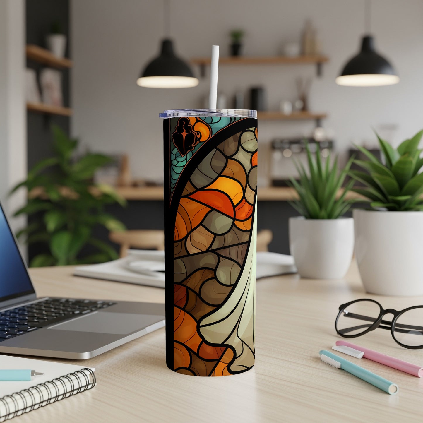 Abstract stained glass tumbler with straw on a desk.