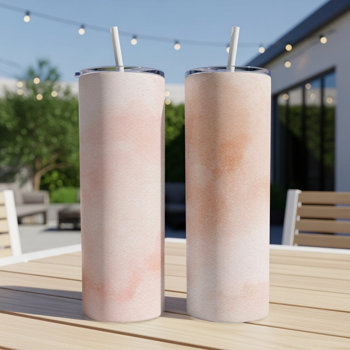 Two tall, pink-washed tumblers with straws on a wooden table outdoors.