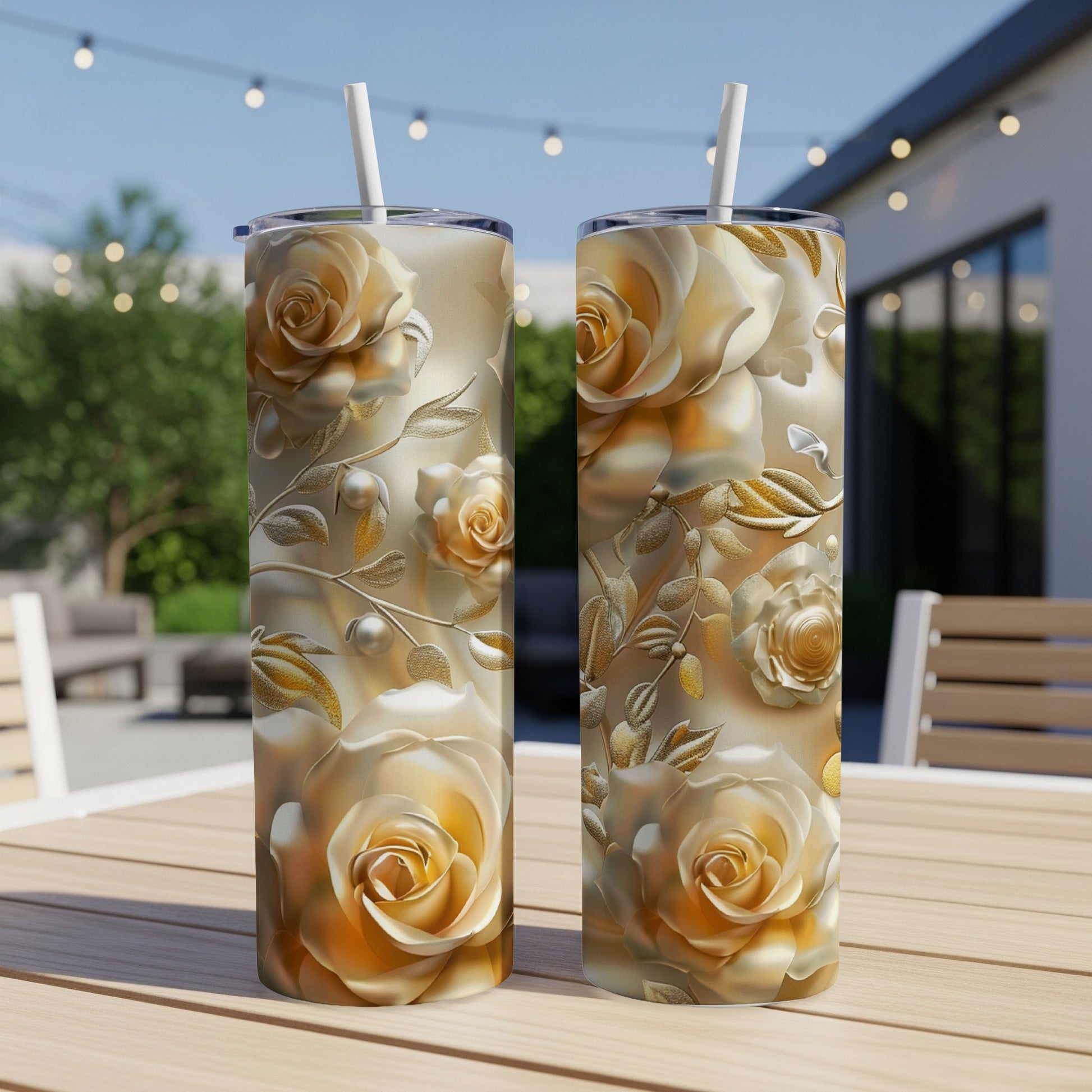 Two tall tumblers with a gold rose floral design on an outdoor table.