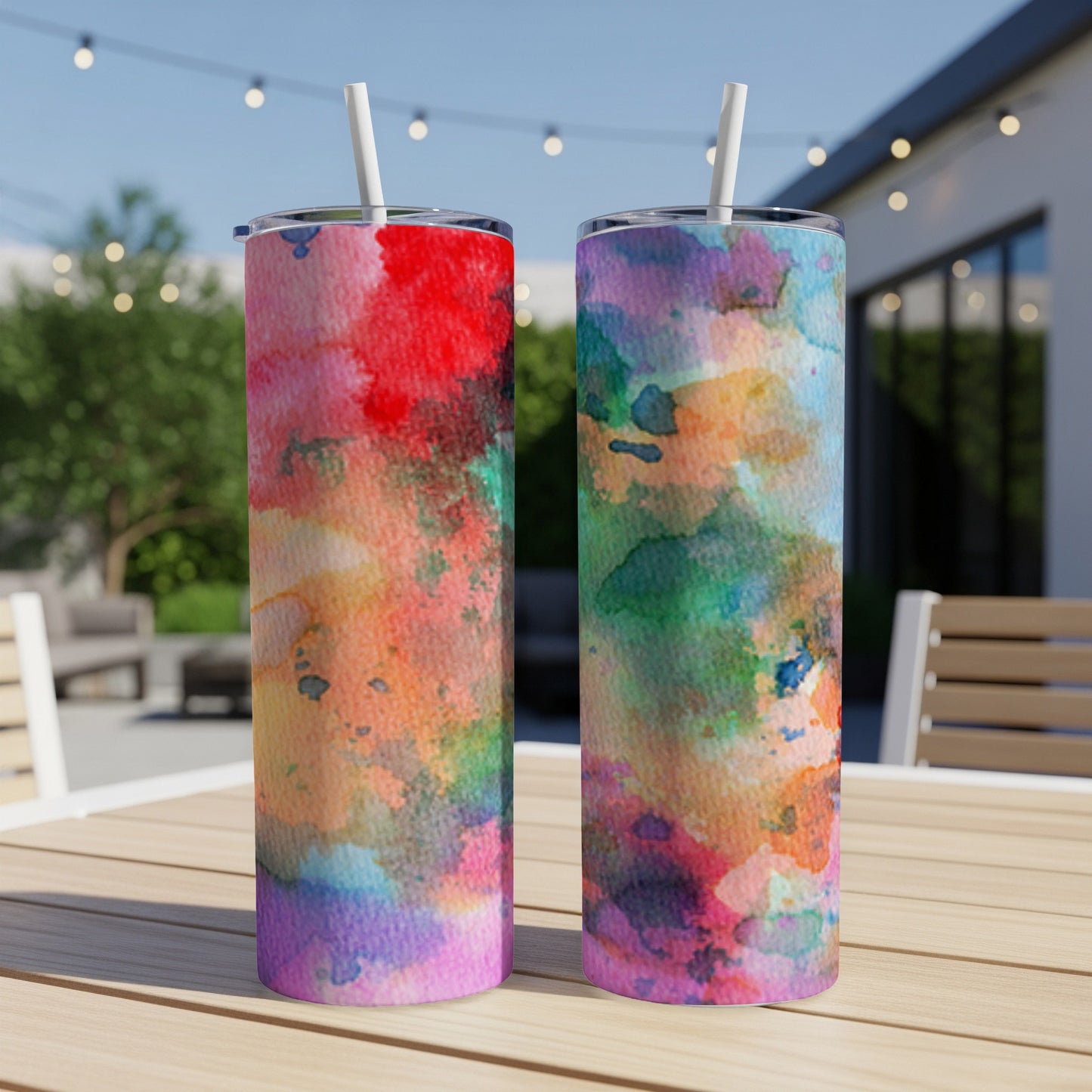Two colorful watercolor tumblers with straws on a wooden table.