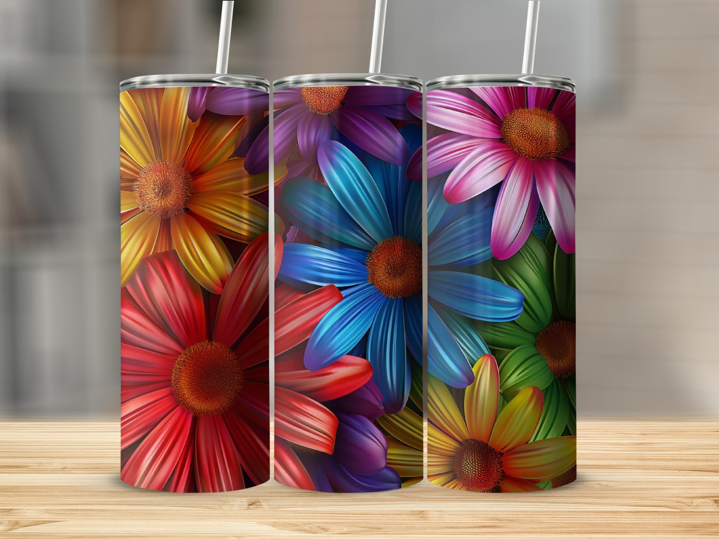 Three floral-patterned tumblers with straws on a wooden surface.