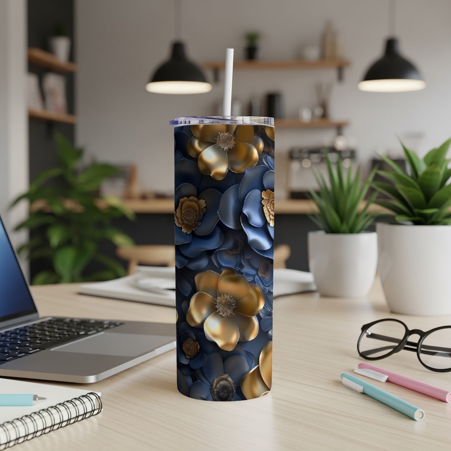 Gold and navy blue floral patterned tumbler with straw on desk.