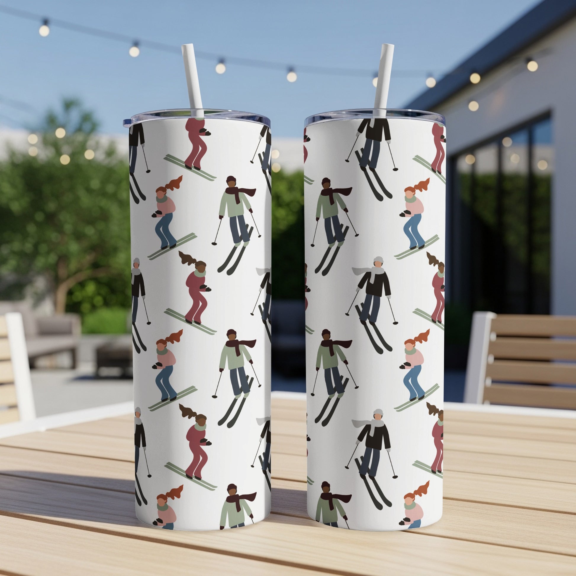 Two white tumblers with repeating pattern of skiers on a table outdoors.